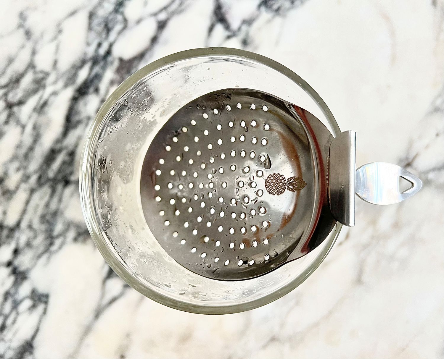 a bent handles strainer in a mixing glass on a marble countertop.