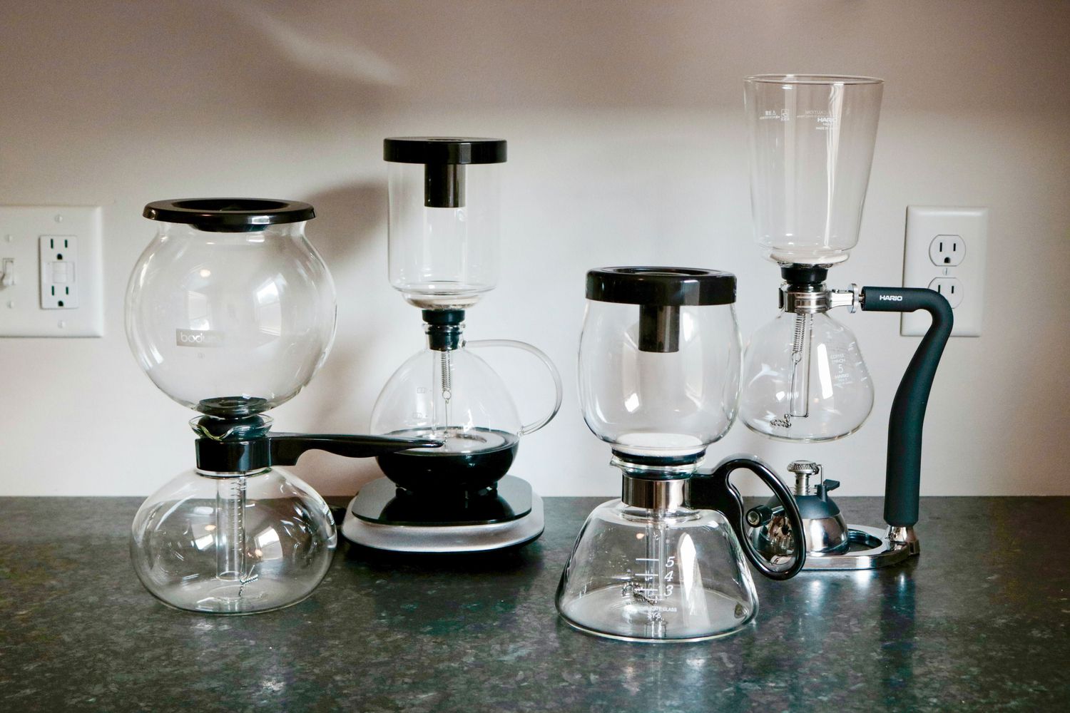 four coffee siphon brewers on a grey surface