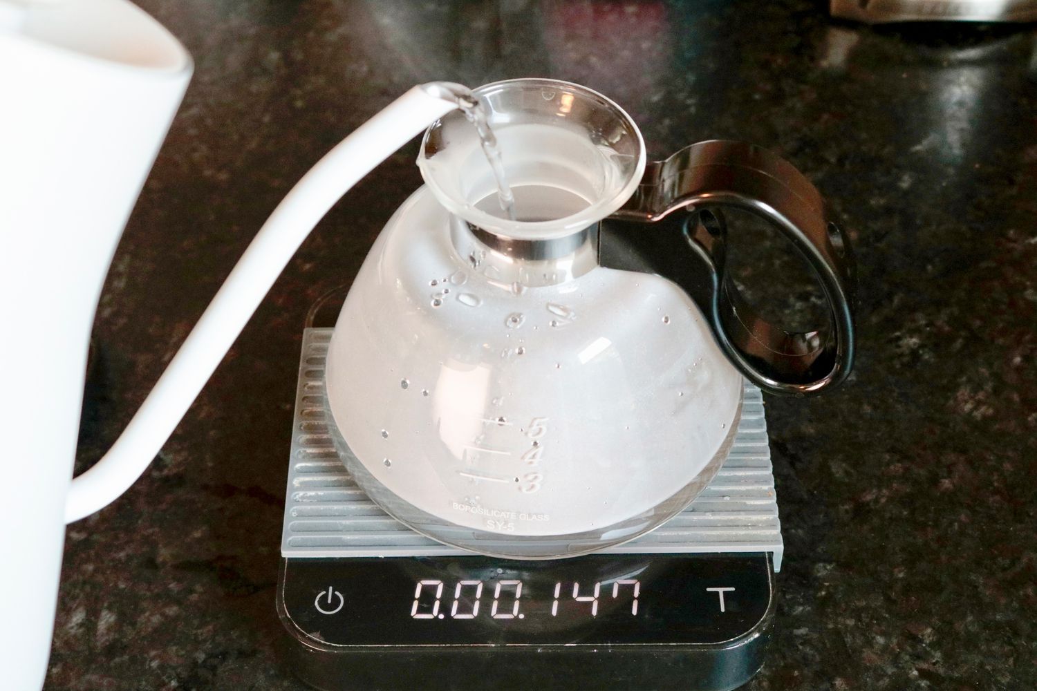 a gooseneck kettle pouring water into a siphon brewer's bottom vessel