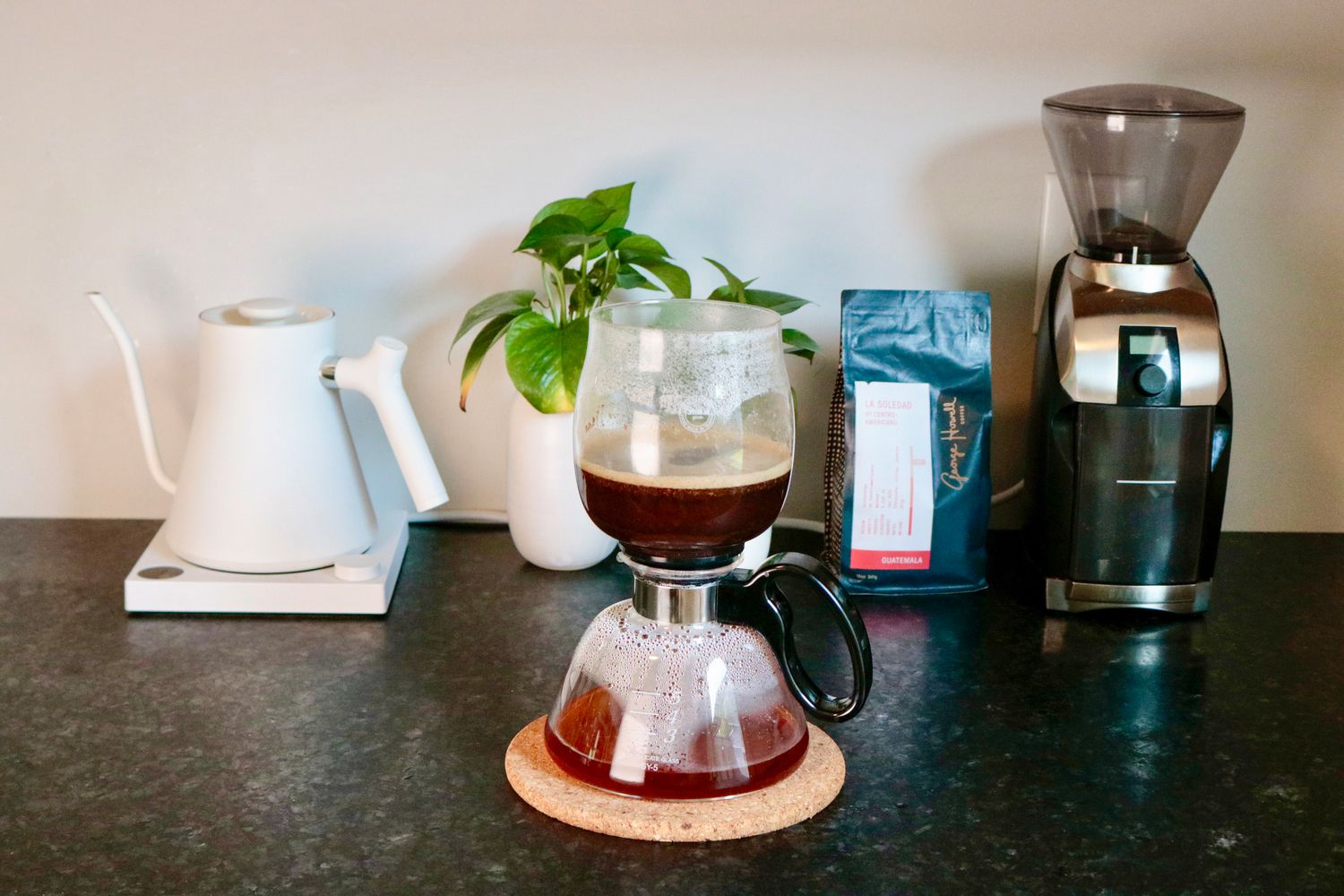 a siphon brewer mid-brew sitting on a cork trivet