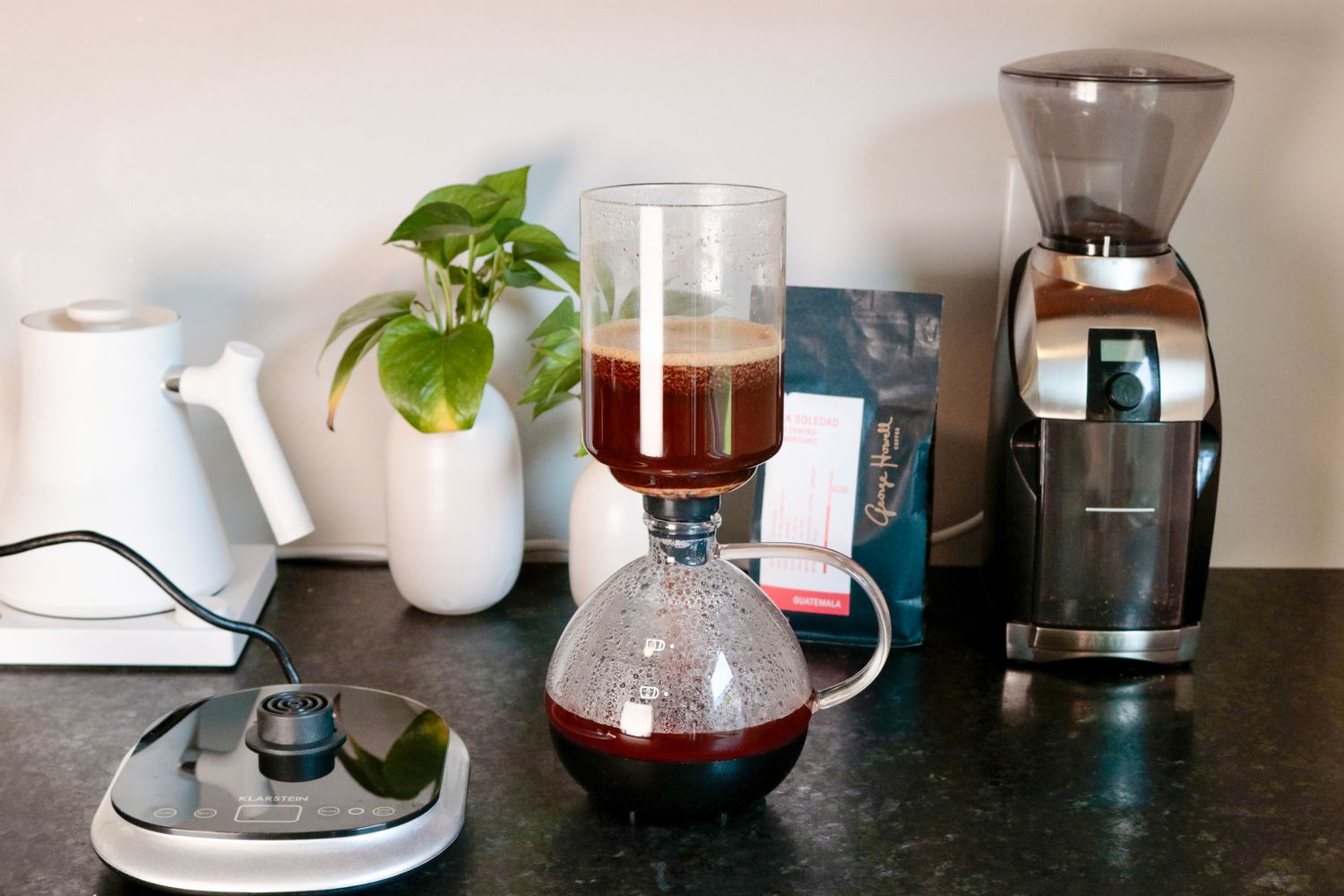 An electric coffee siphon full of coffee and set beside its electronic base