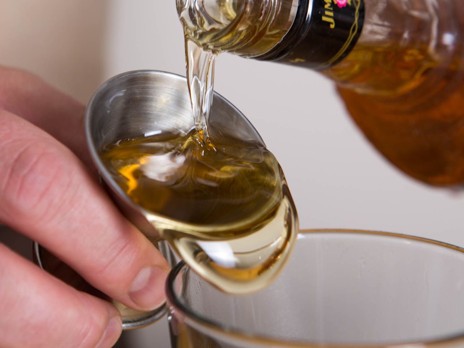 pouring a spirit into a jigger and that jigger overflowing into a measuring glass