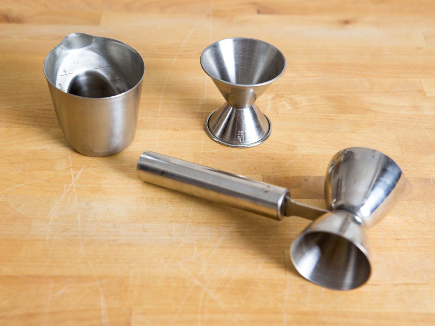 three types of stainless steel jiggers on a wooden surface