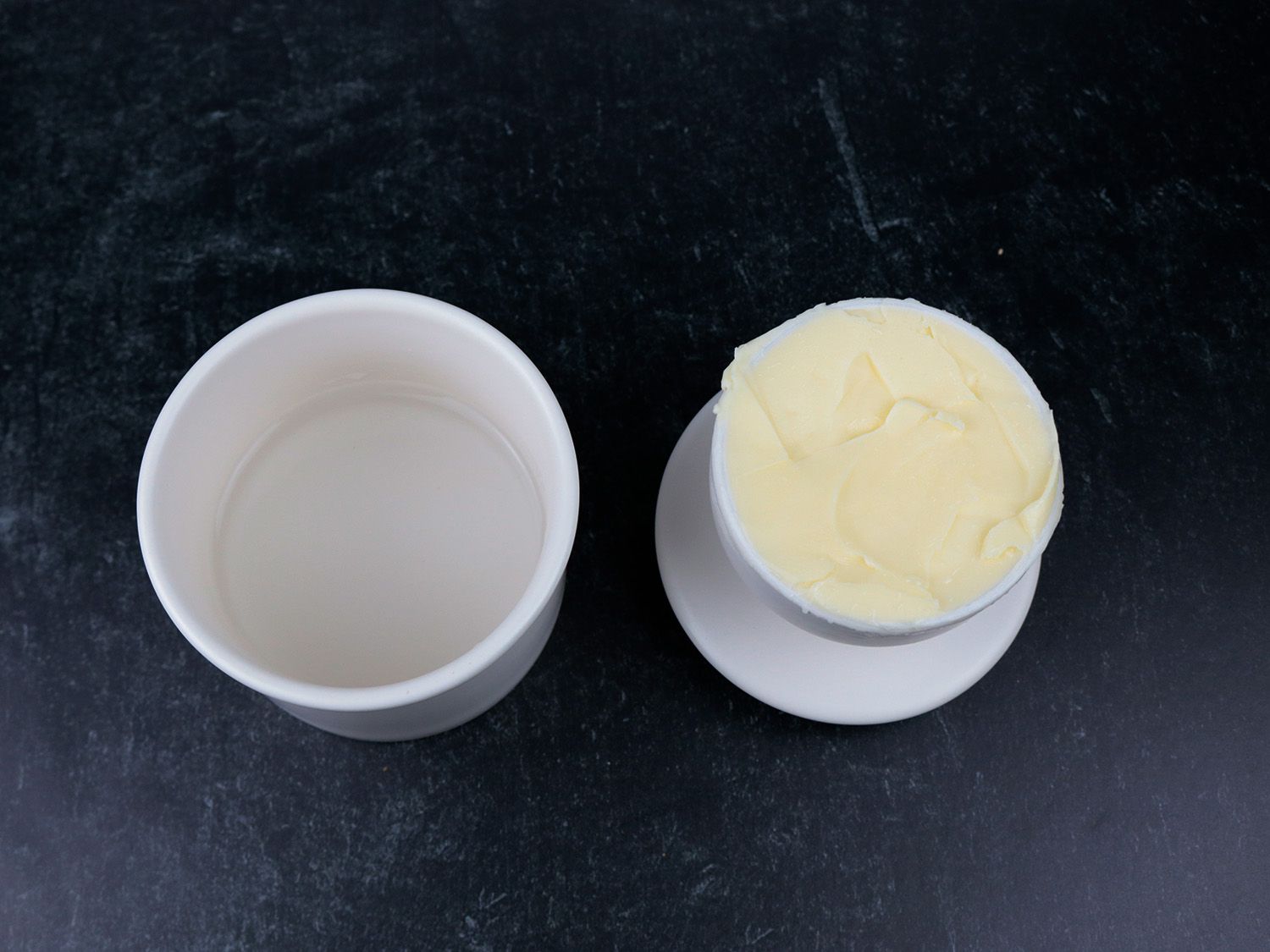 two sides of a ceramic butter crock rest on a counter showing water in one half and butter in the other
