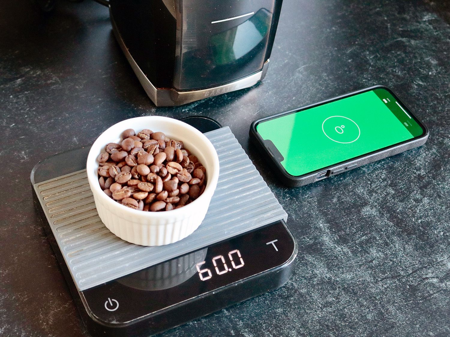 a phone with a level application showing the counter is level next to a scale with coffee weight out on it