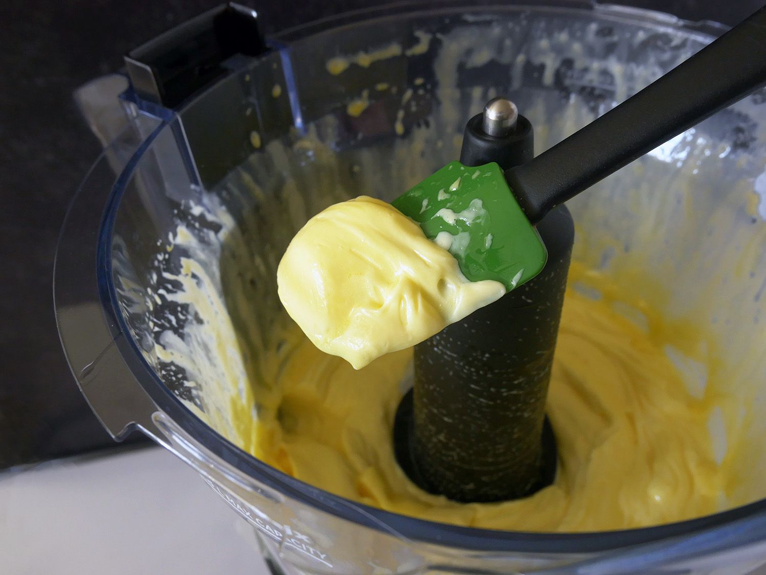 a closeup shot of a spatula scooping mayonnaise out of the vitamix food processor.