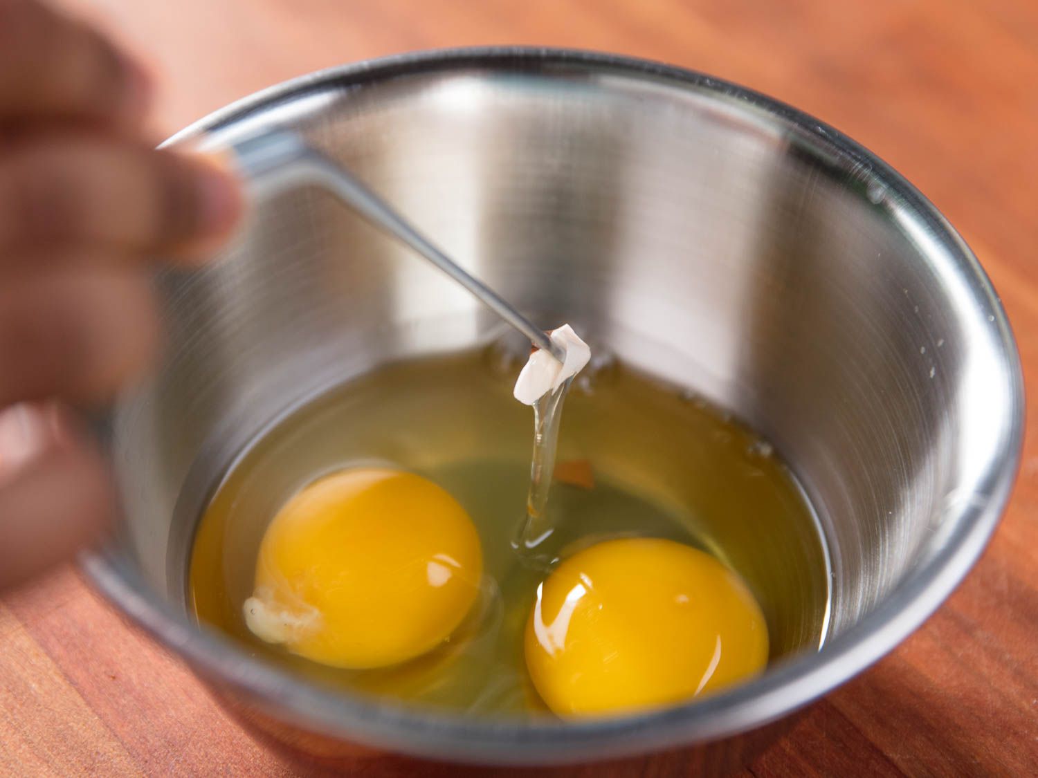 tweezer picking a piece of eggshell out of a bowl with eggs in it