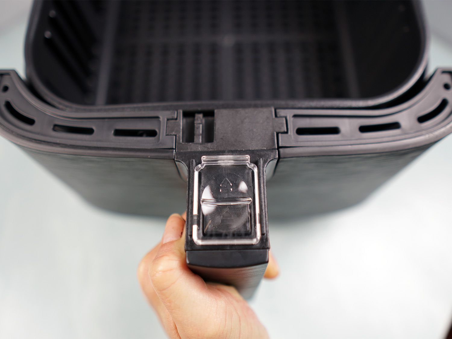 a closeup look at a handle of an air fryer with a plastic cover over its basket release button