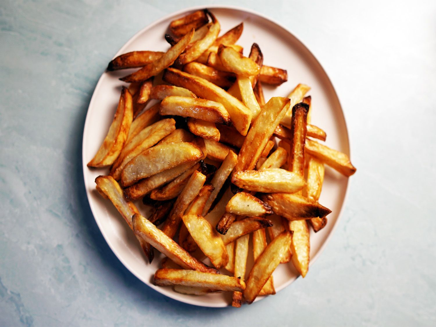 a plate of air-fried french fries on a blue surface