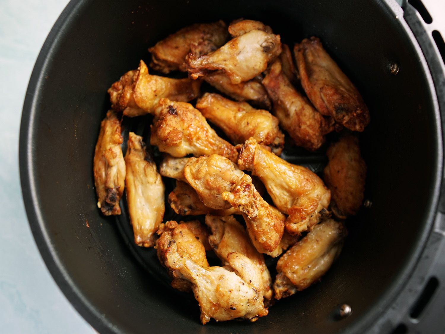 A round air fryer basket filled with cooked chicken wings