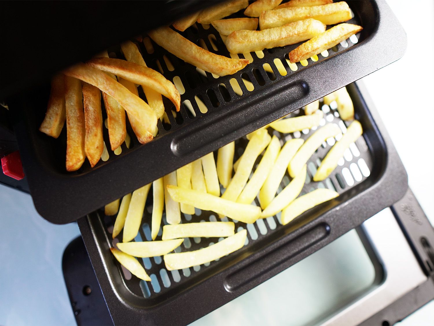 a double layer, tray air fryer with one tray holding browned fries and another holding uncooked fries