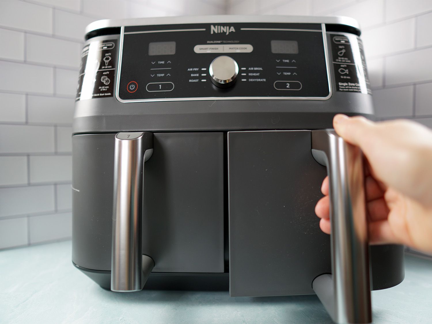 A hand pulling out the basket of a dual-basket air fryer