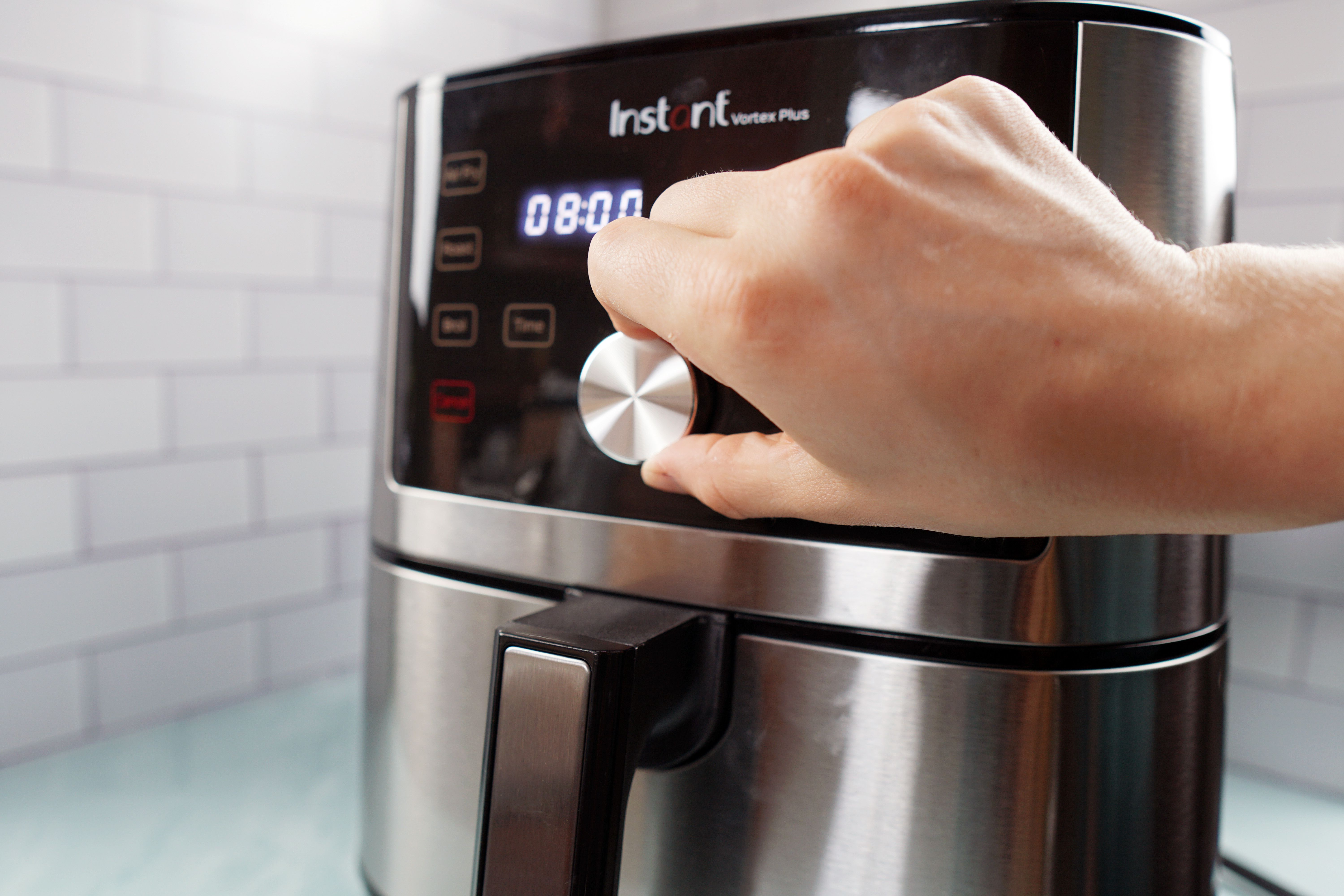 A hand turning the control knob to adjust the temperature on an air fryer