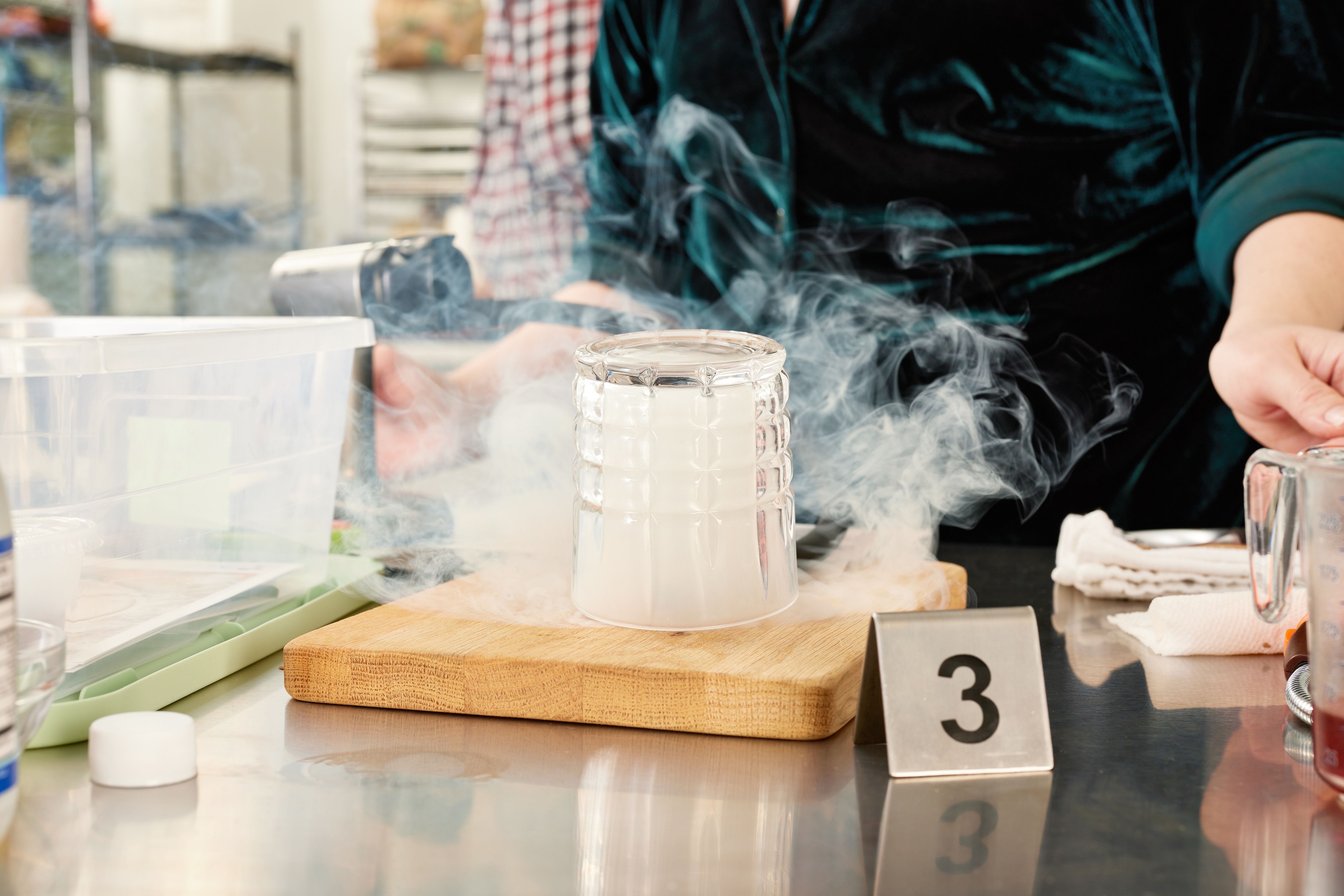 a person standing behind a cocktail smoker as smoke billows out of a smoking cloche