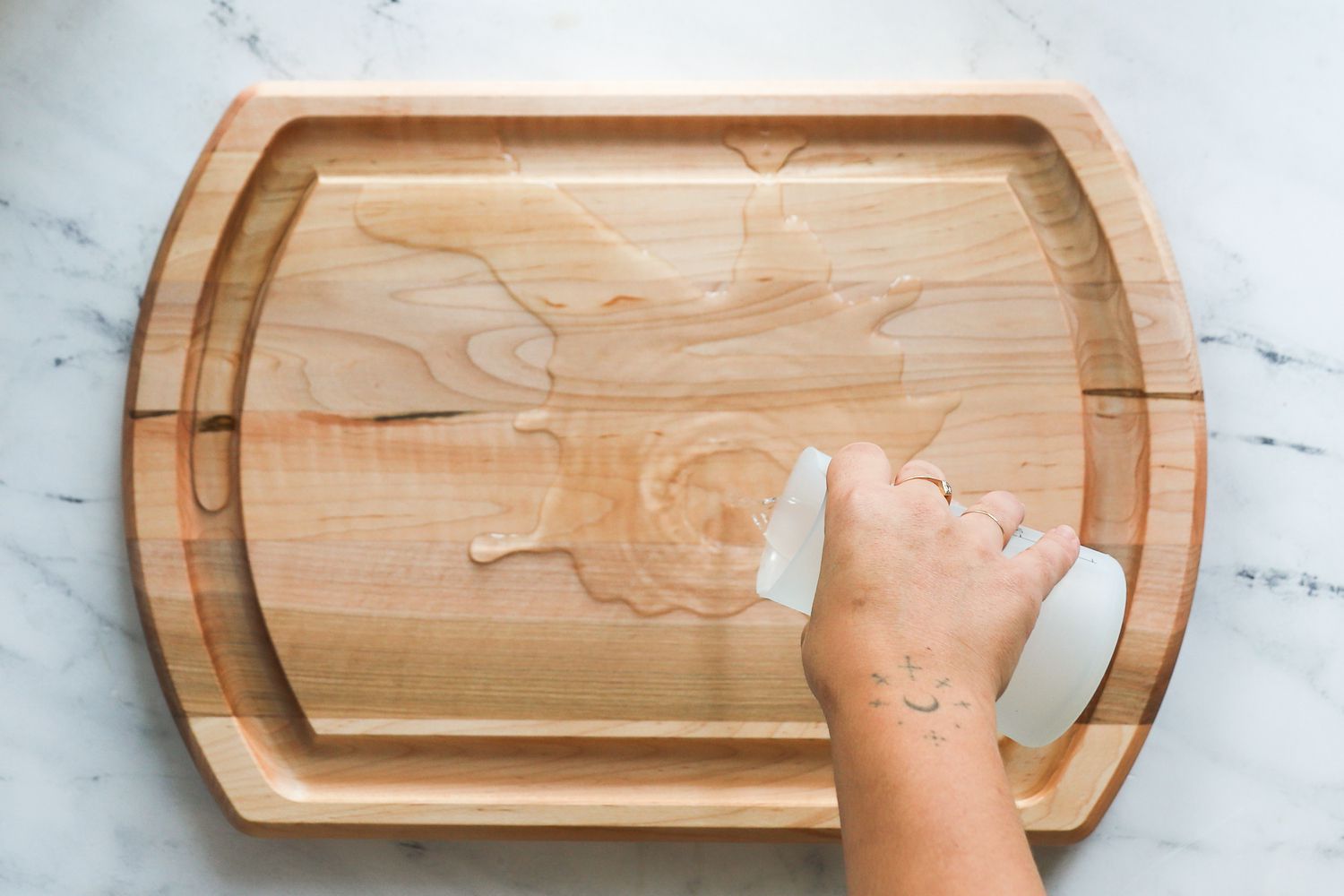 A hand pouring water into the center of a carving board