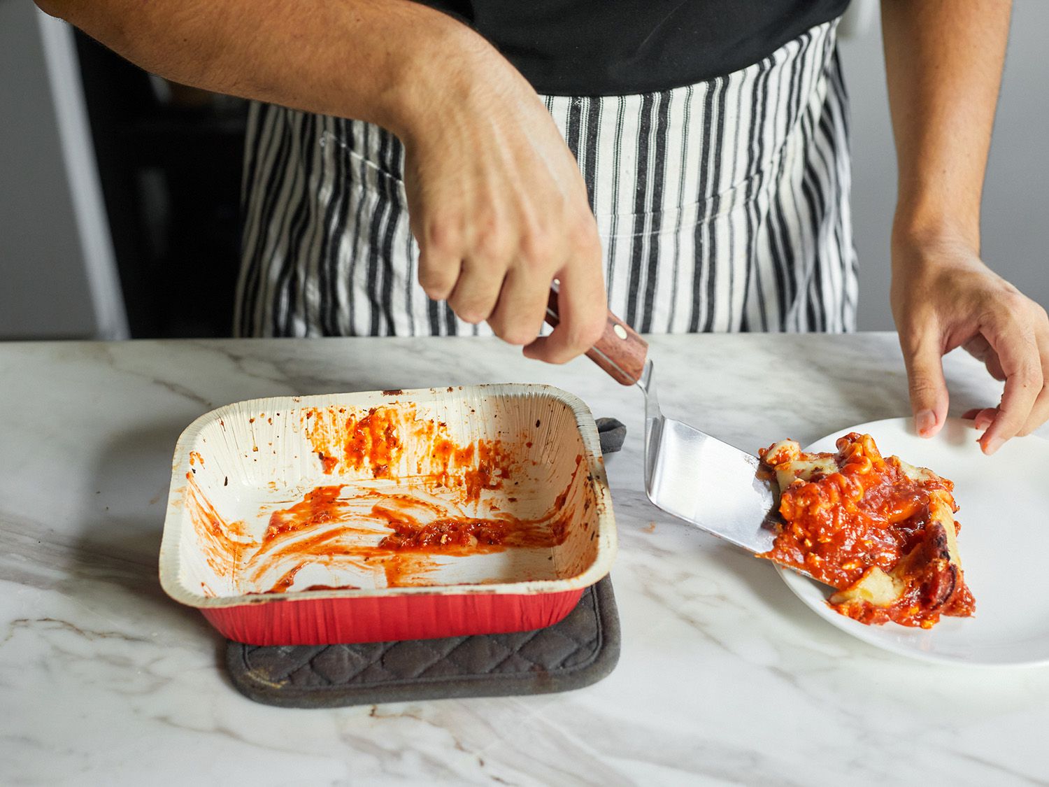 someone using an offset metal turner to serve a piece of lasagna