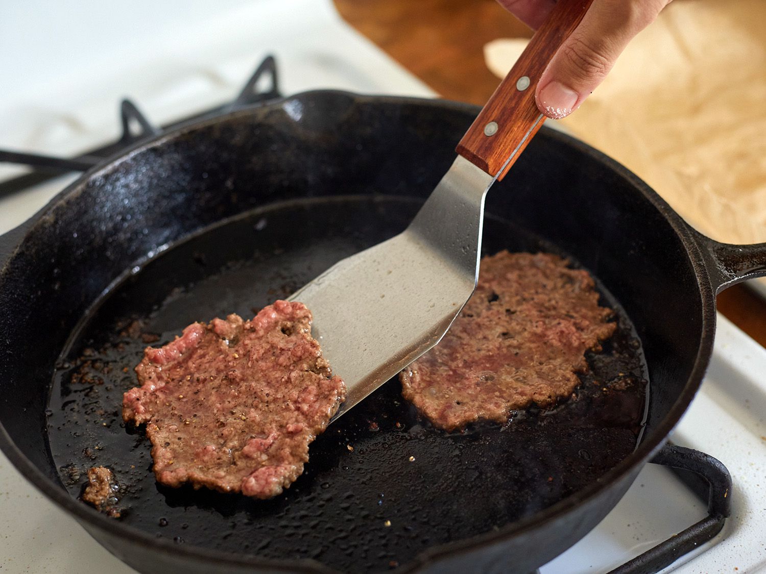 an offset metal turner lifting a smash burger from a cast iron skillet.