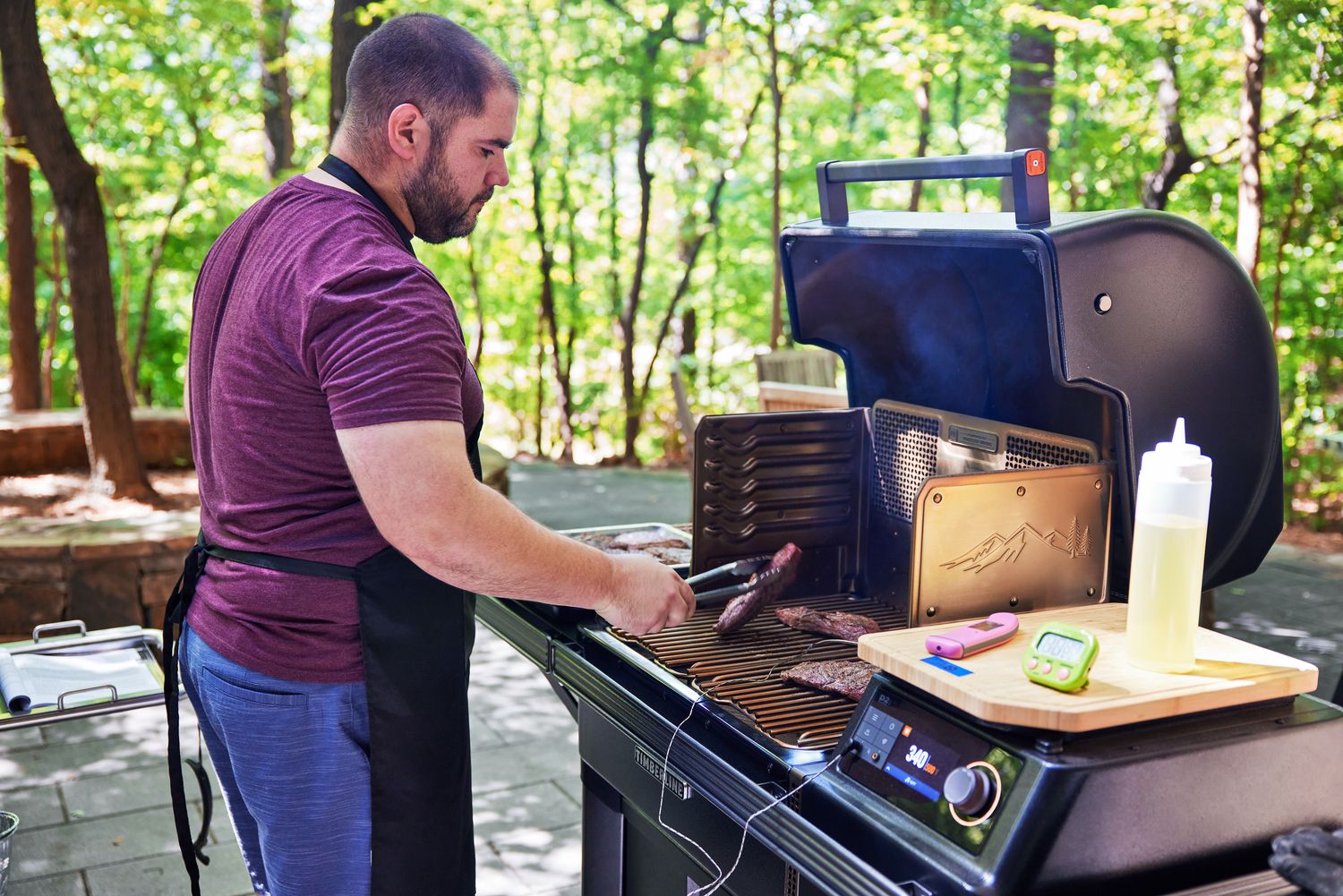A person using tongs to flip a piece of a meat on a Traeger grill