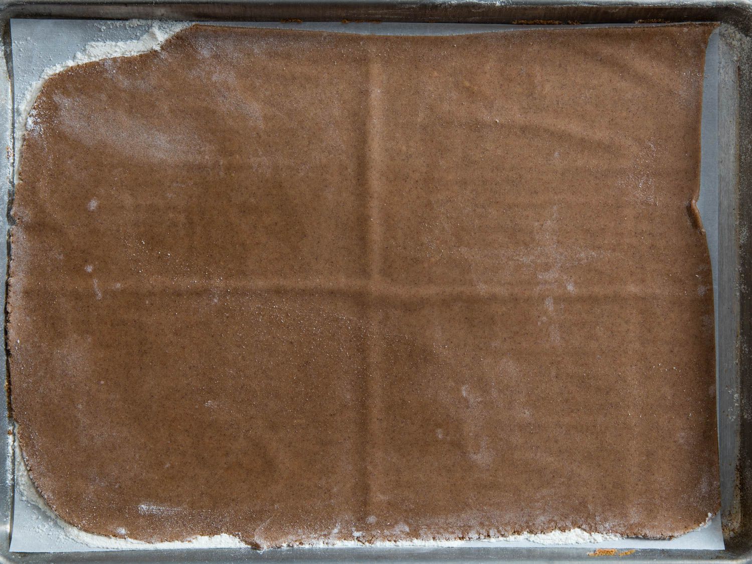 a sheet of gingerbread on parchment paper set in a sheet pan