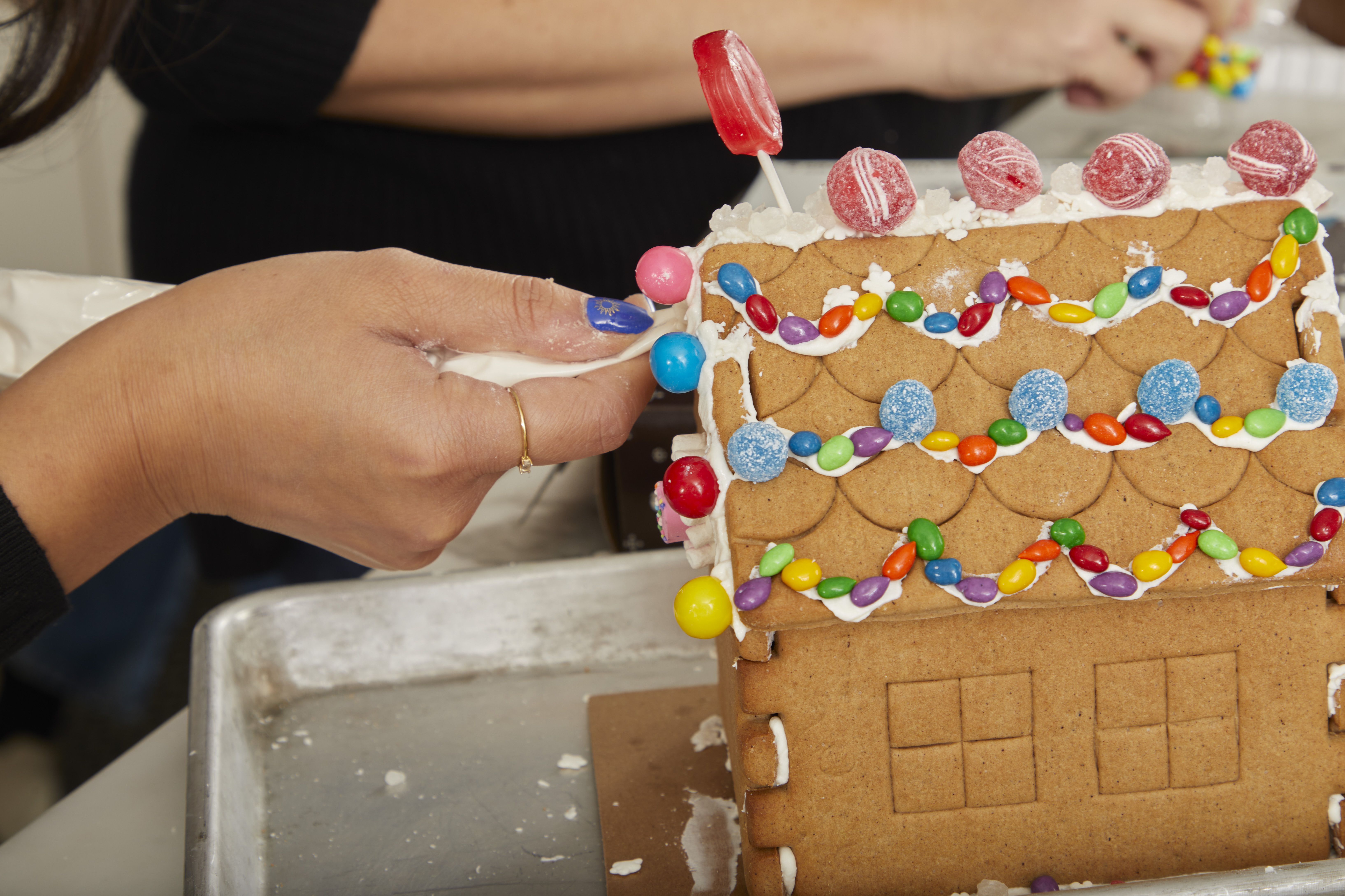 A person using icing to decorate a gingerbread house