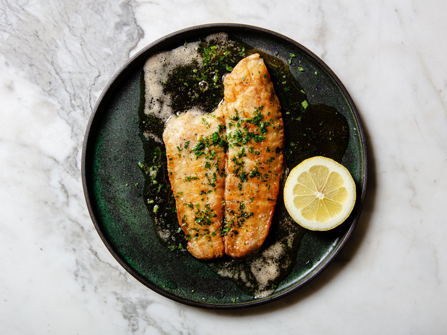 Sole Meuniere on a dark green plate on a marbled countertop