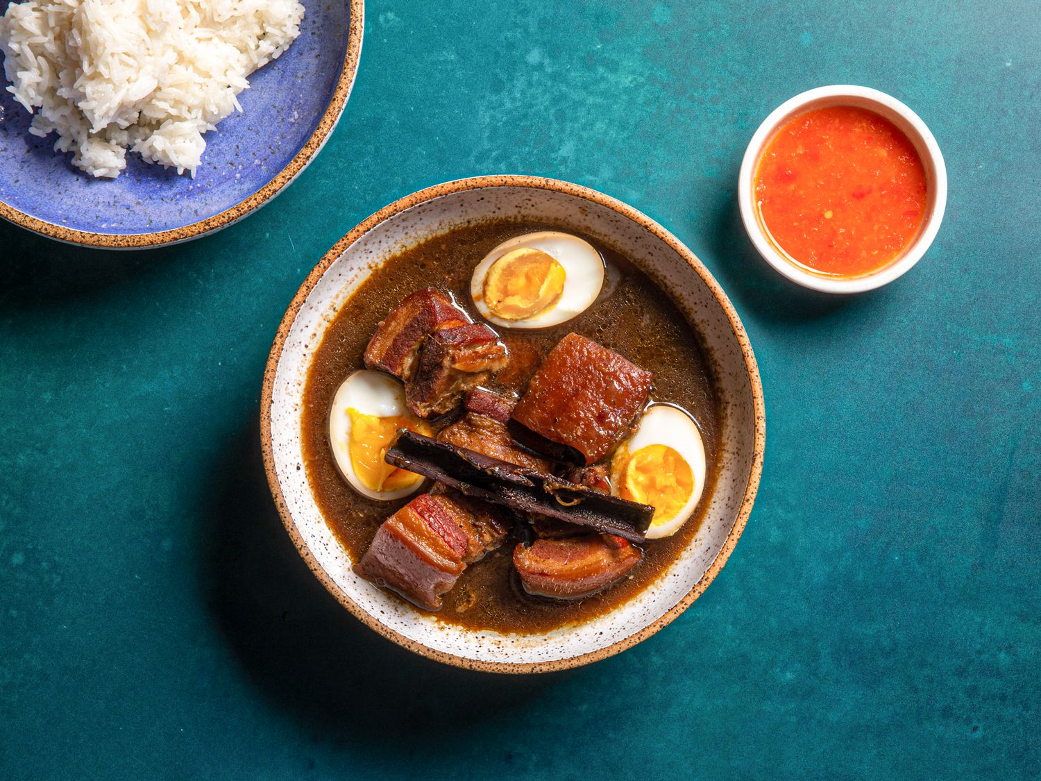 Overhead shot of finished moo palo with cut open eggs, dipping sauce, and a plate of rice