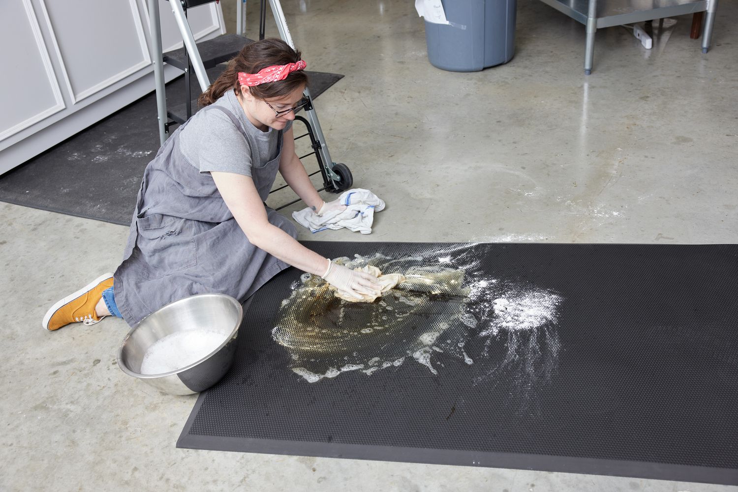 A person sitting on the ground and cleaning a kitchen mat with soapy water