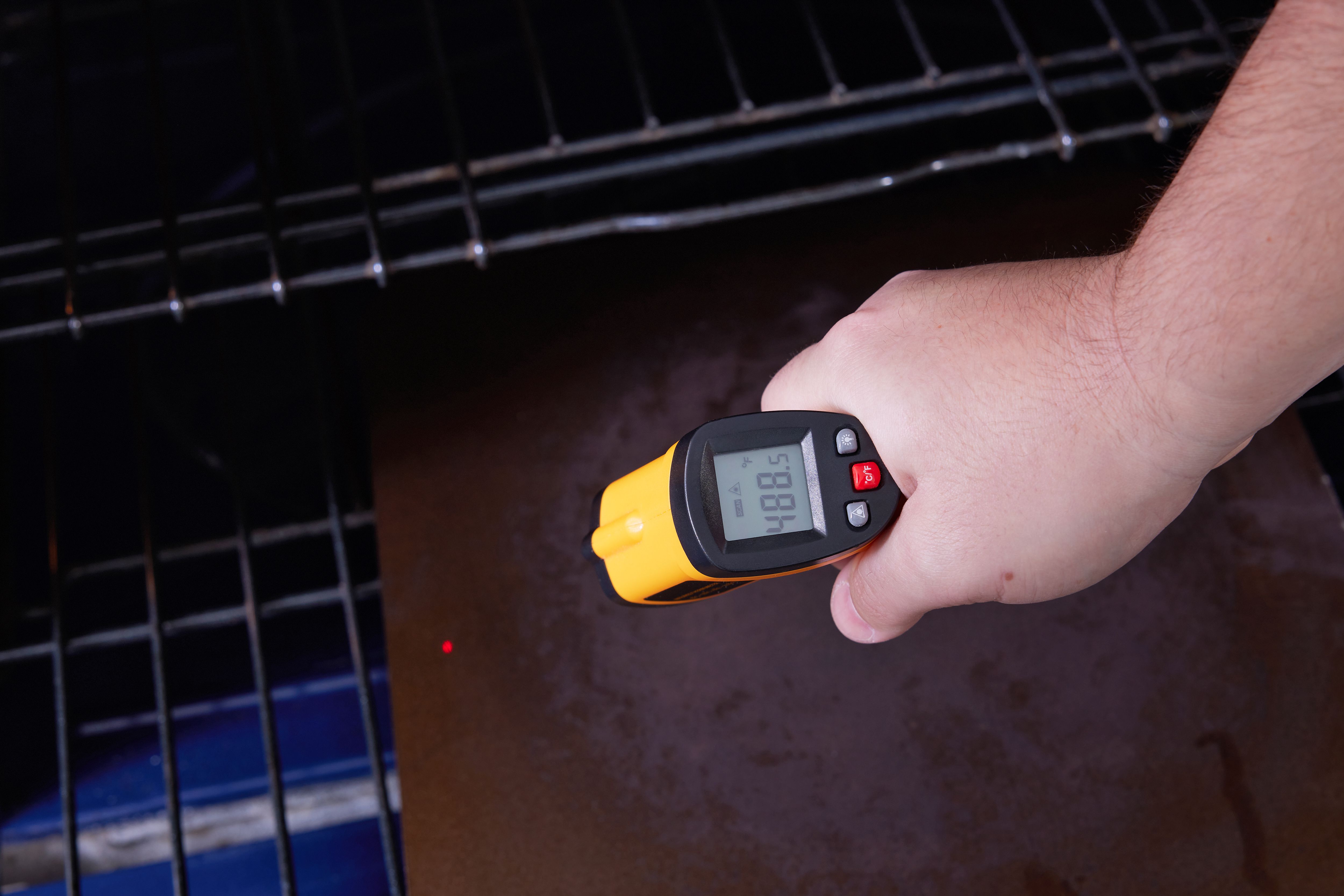 A hand using an infrared thermometer to take the temperature of a baking steel in the oven