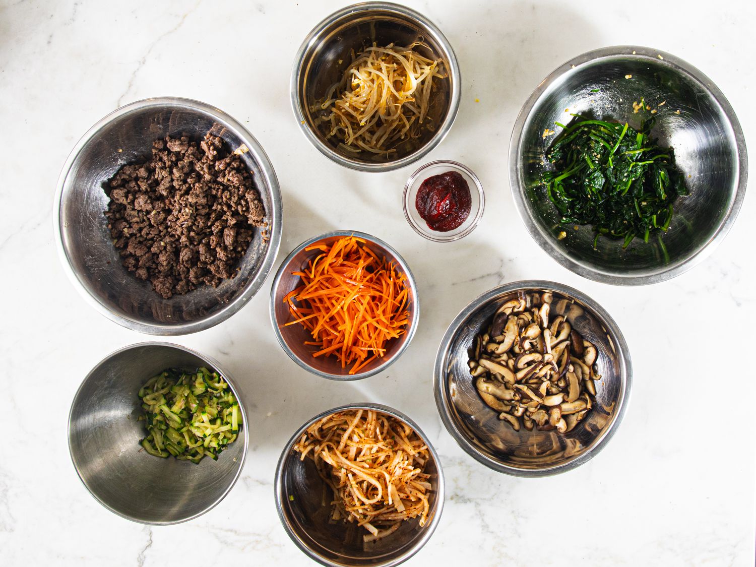 Overhead view of toppings of bibimbap in metal bowls