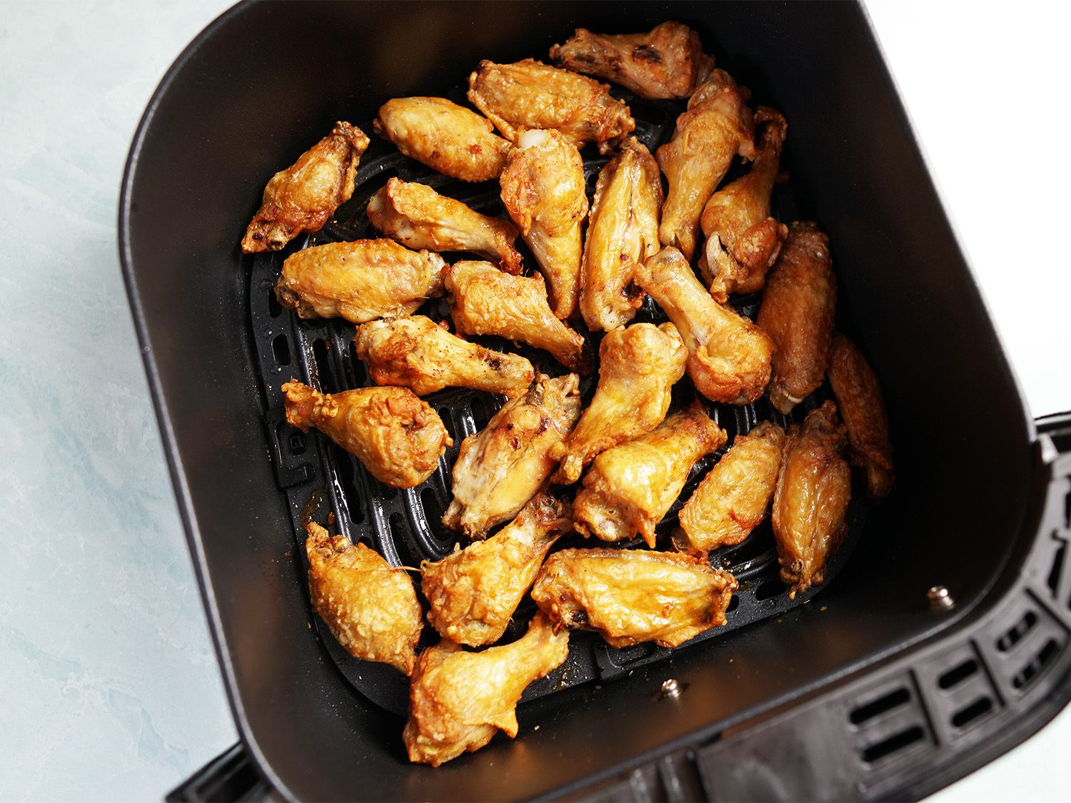 An air fryer basket filled with browned, cooked chicken wings