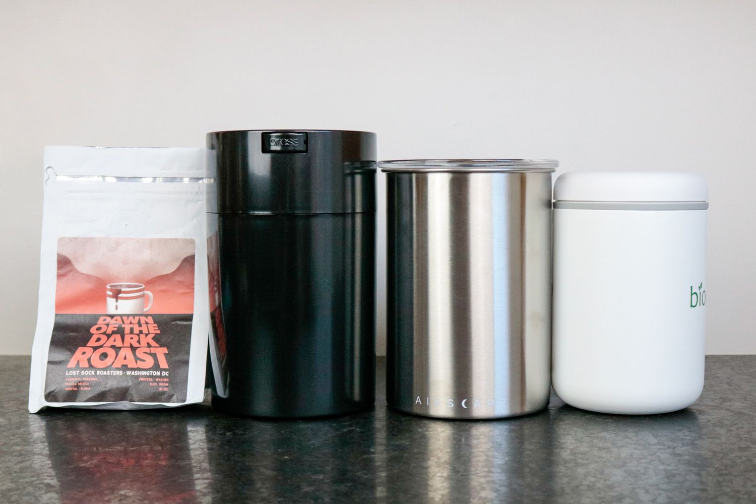 Three coffee storage containers and a coffee bag on a grey countertop