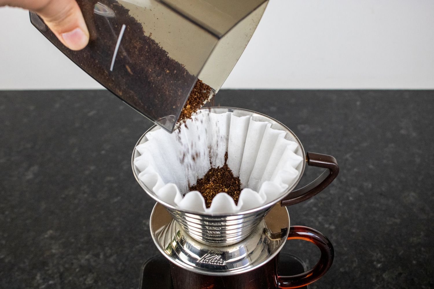 A hand pouring ground coffee into a pour over coffee maker's filter