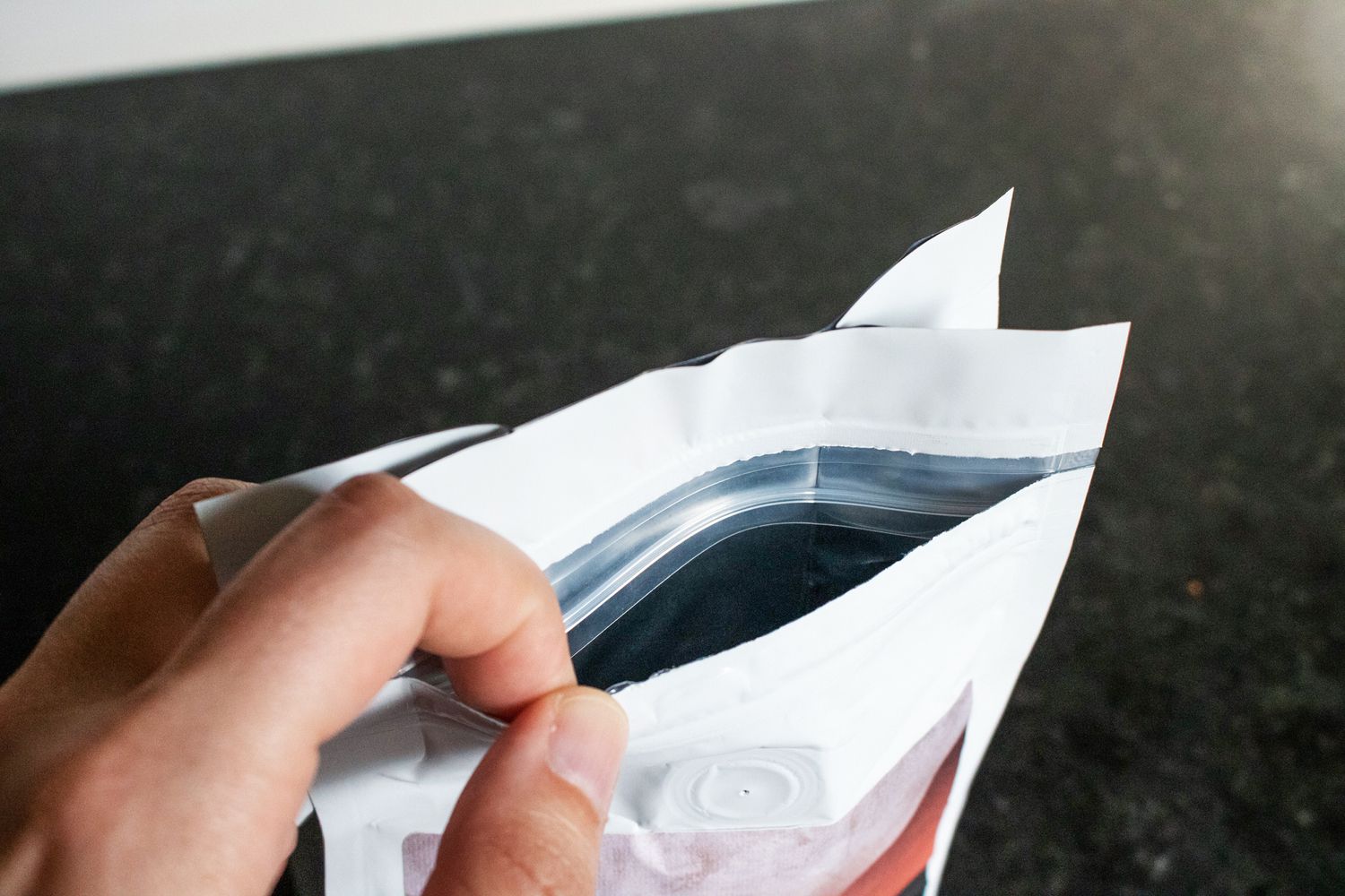 A hand holding a coffee bag open