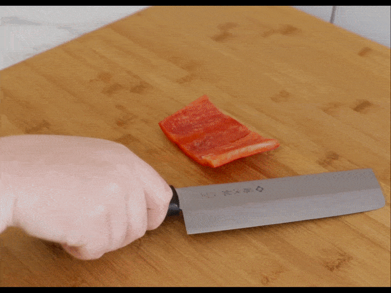 A video of a person using a nakiri knife to cut a red bell pepper into strips, then dice it