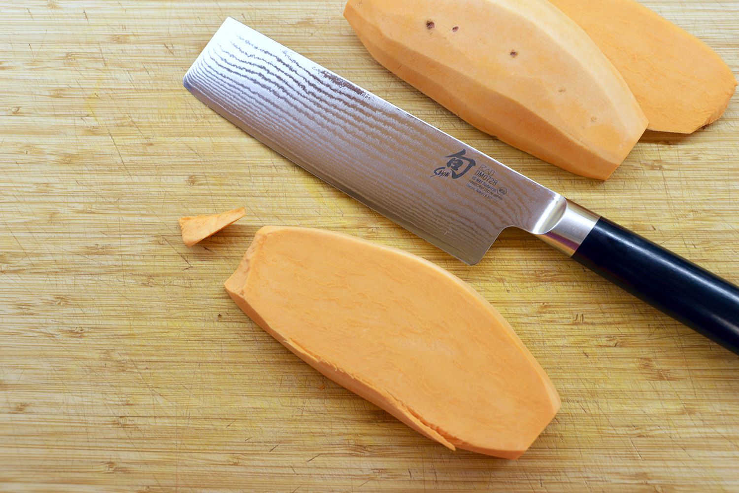 A nakiri knife on a wooden cutting board with slices of sweet potato surrounding it