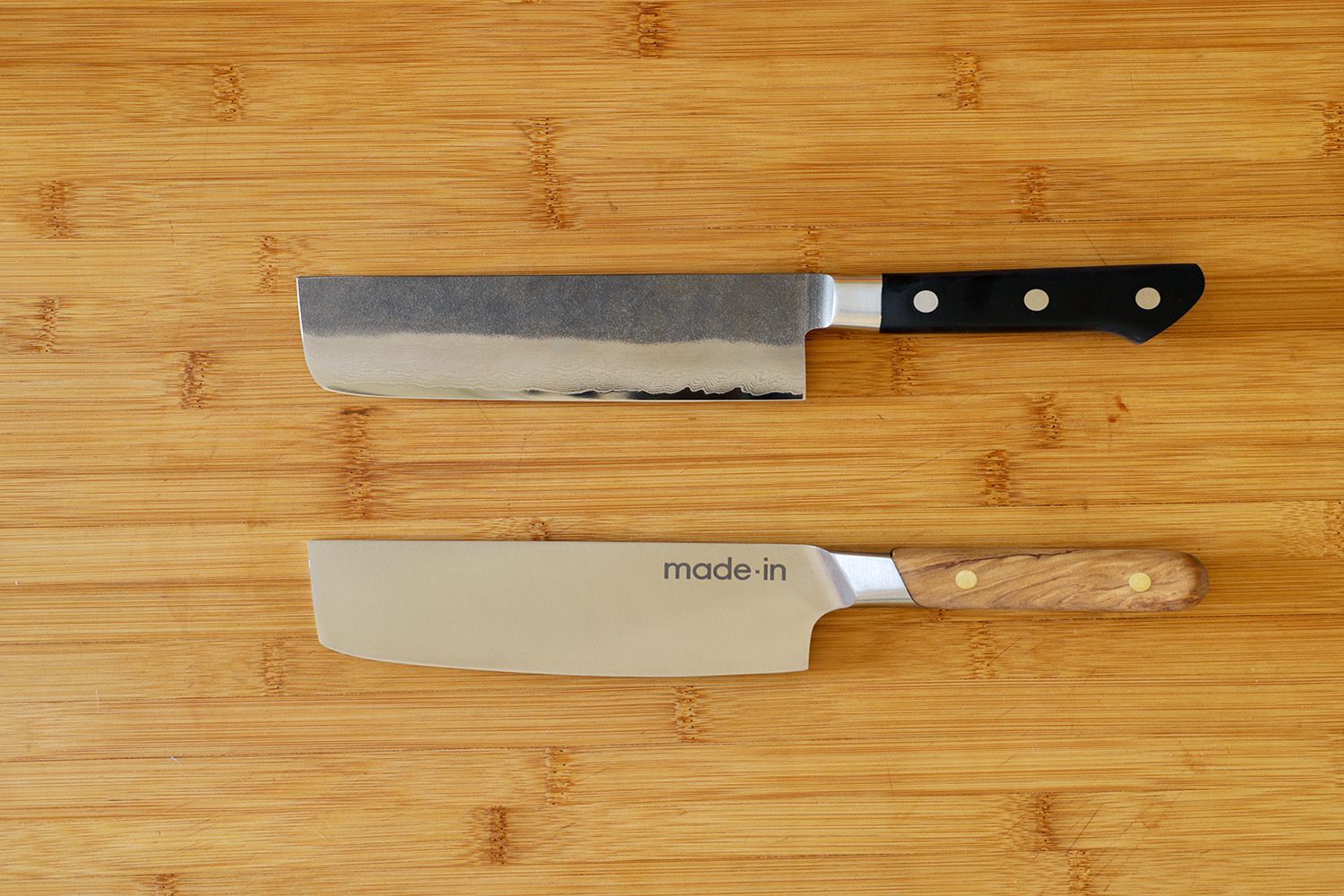 Two nakiri knives lying horizontally on a wooden surface