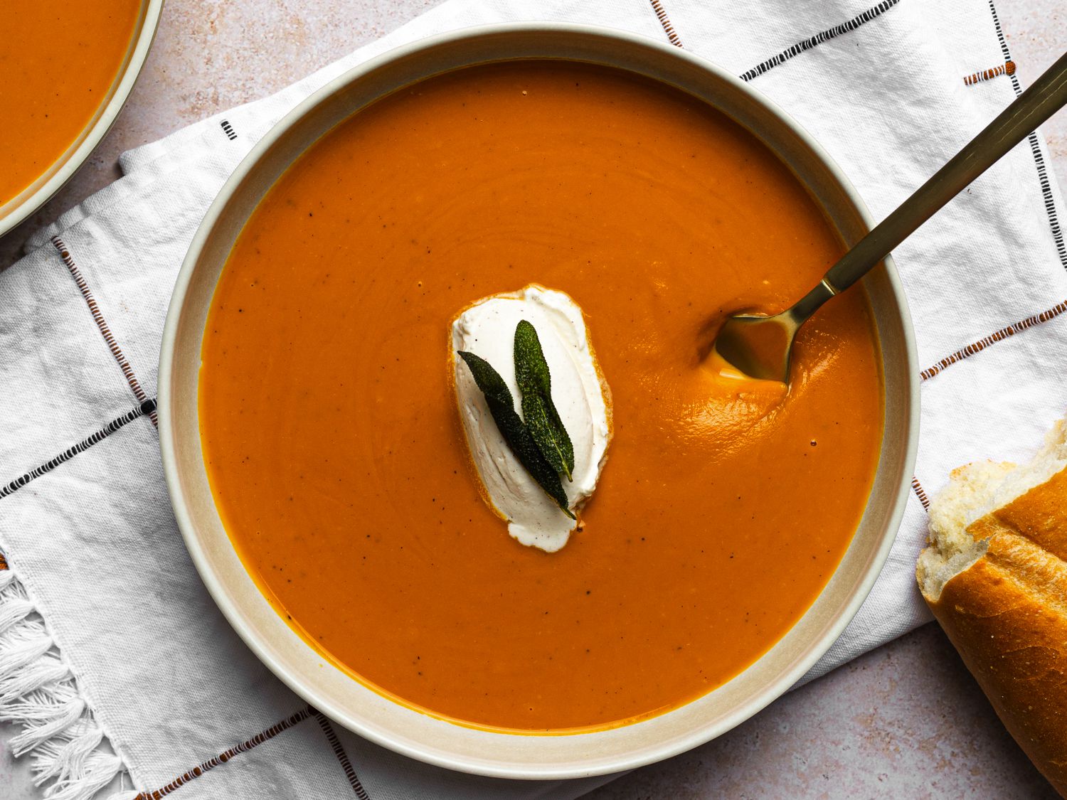 A bowl of butternut squash soup on a dish towel. There is a metal spoon in the bowl.