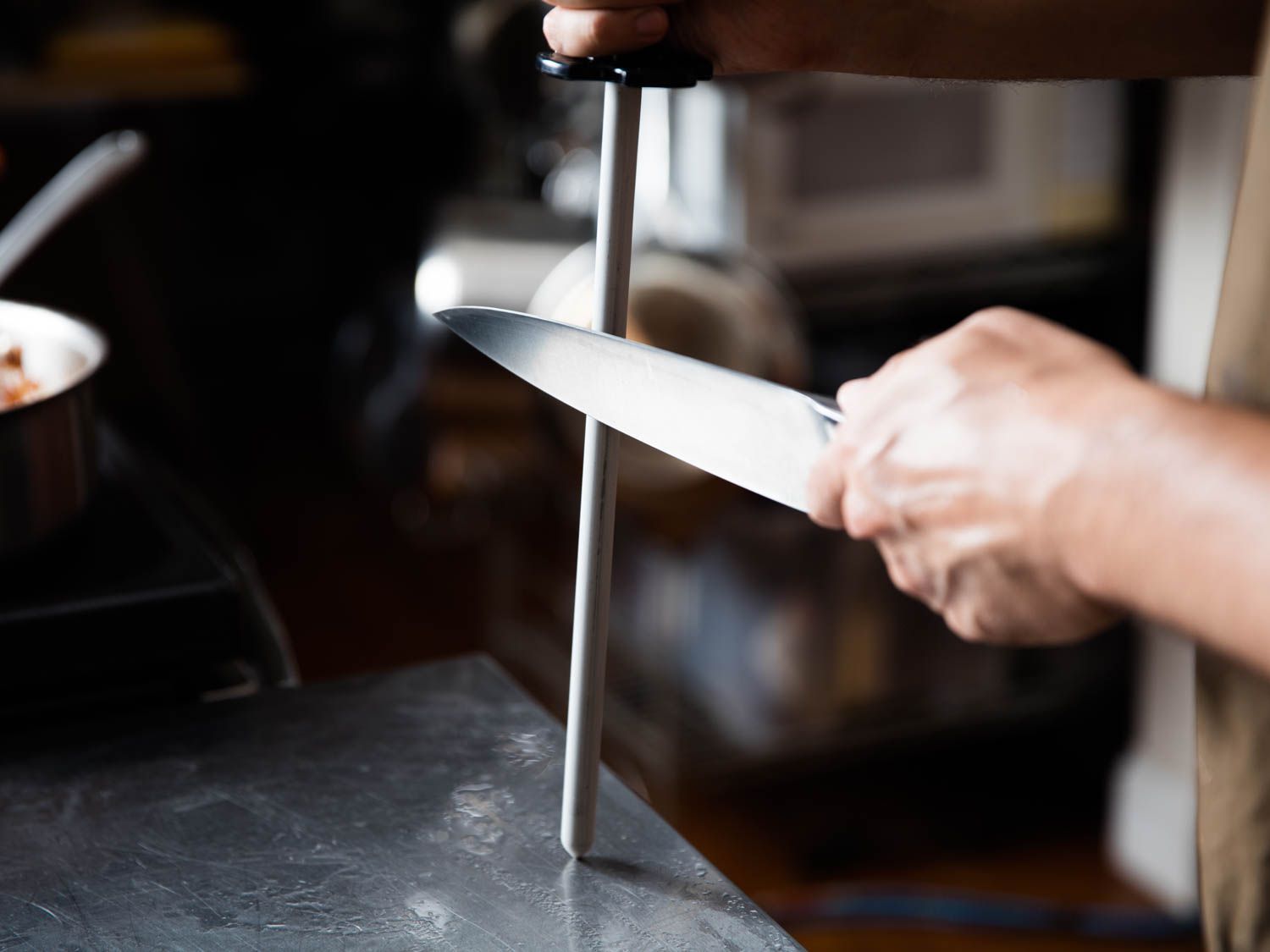 a hand holding a honing rod and running a chef's knife down it