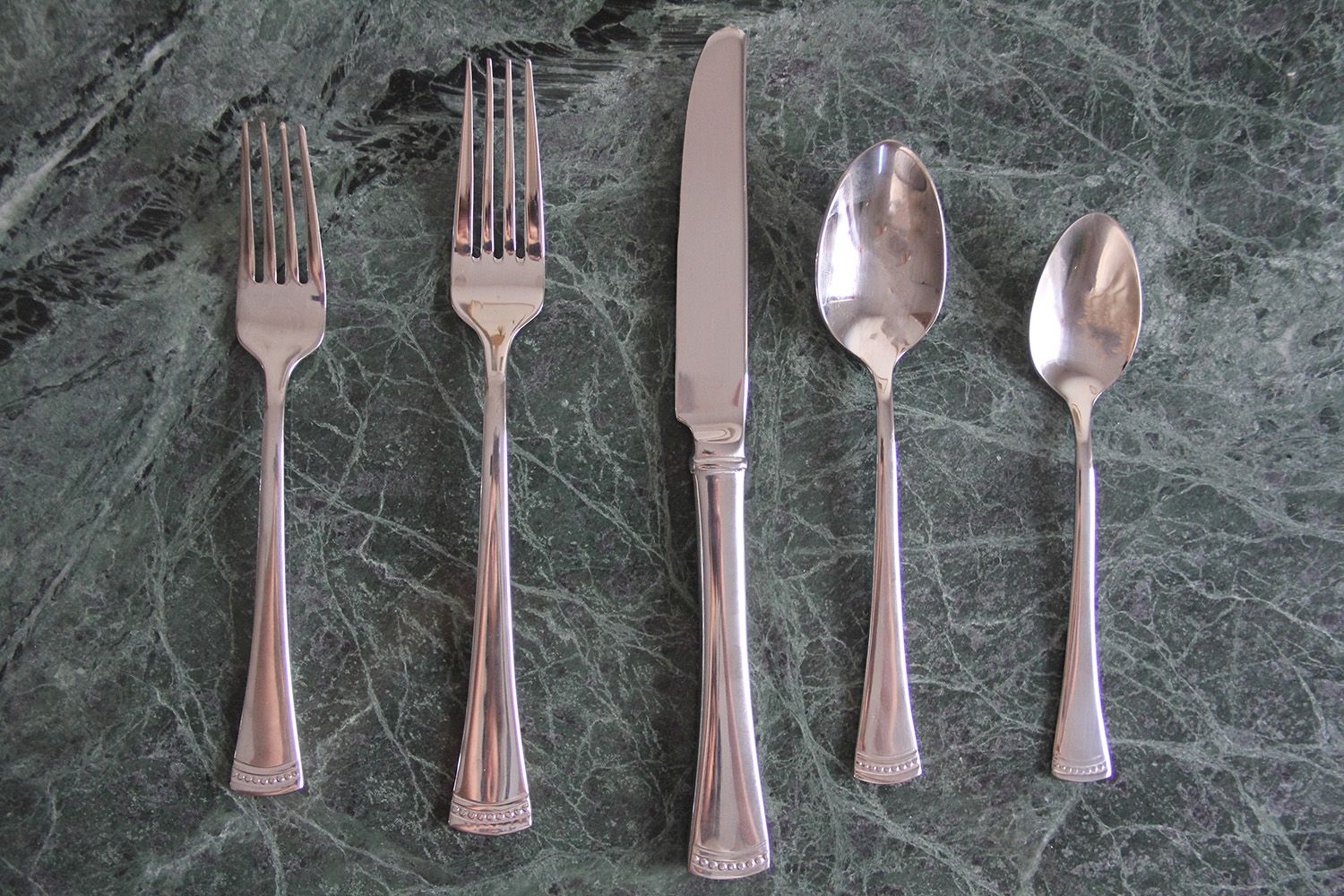 a set of stainless steel silverware on a marble surface