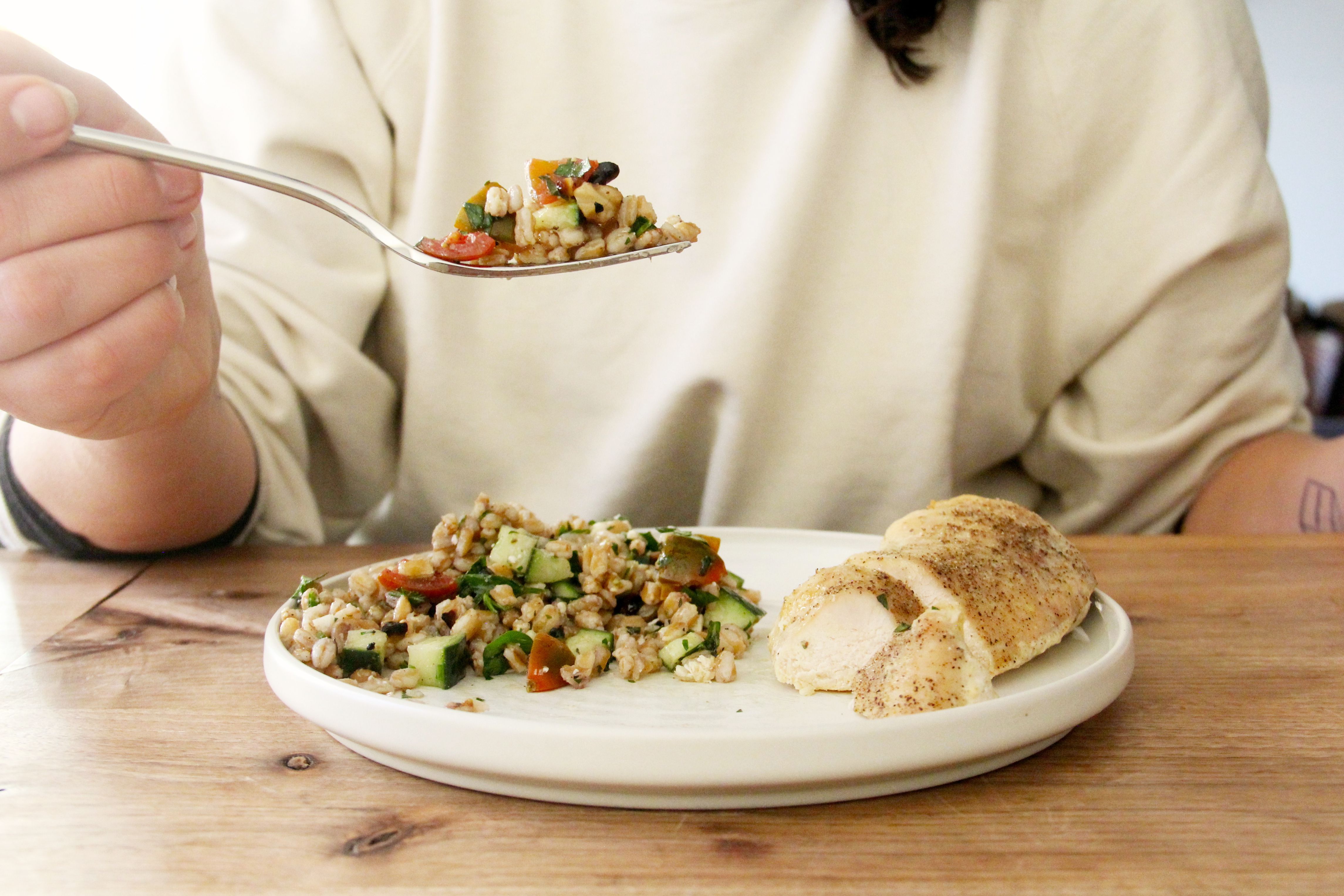 a person holding a forkful of grain salad up and above a plate