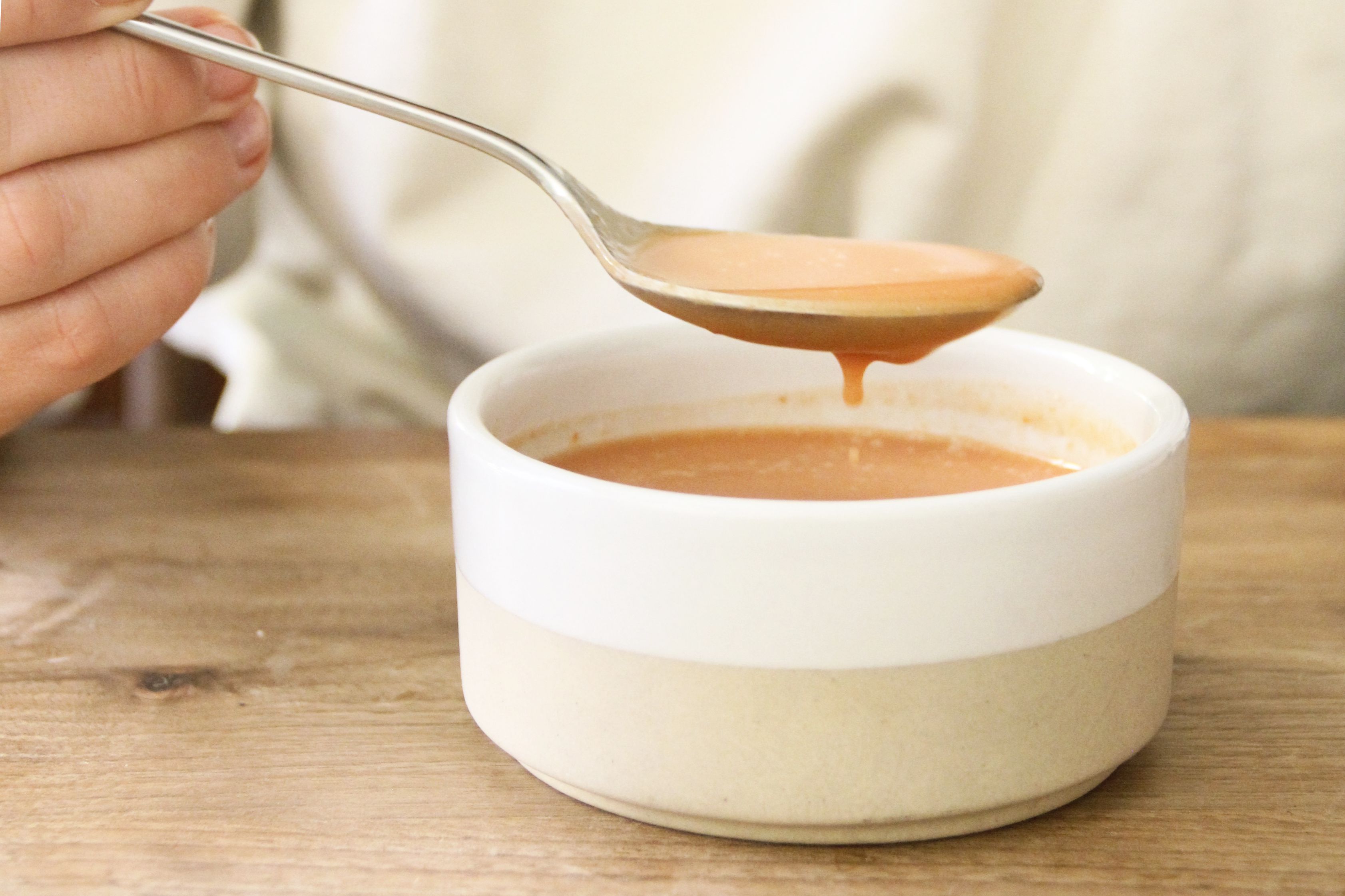 A person holding a spoon full of tomato soup above a bowl of tomato soup