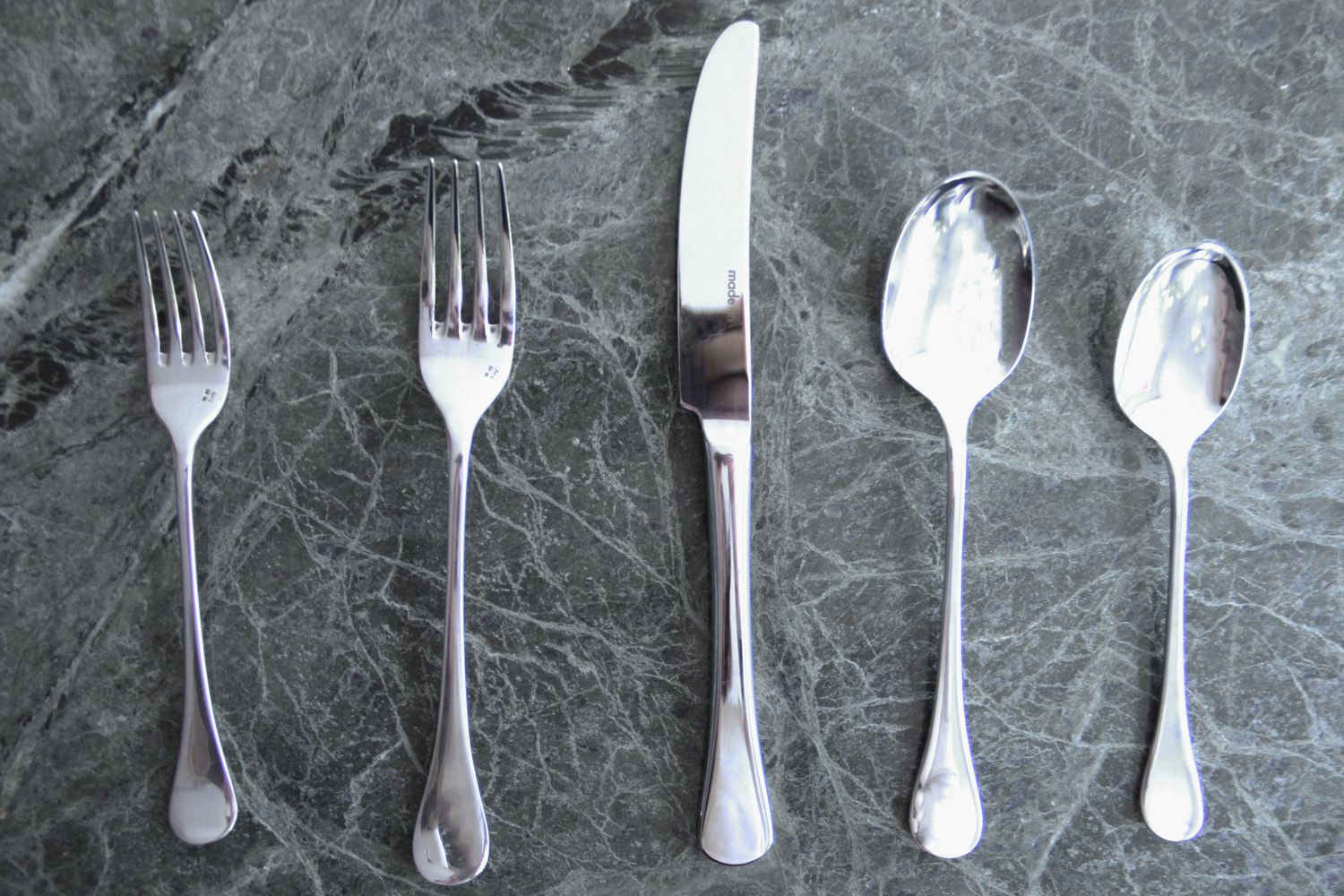A stainless steel silverware set on a grey surface