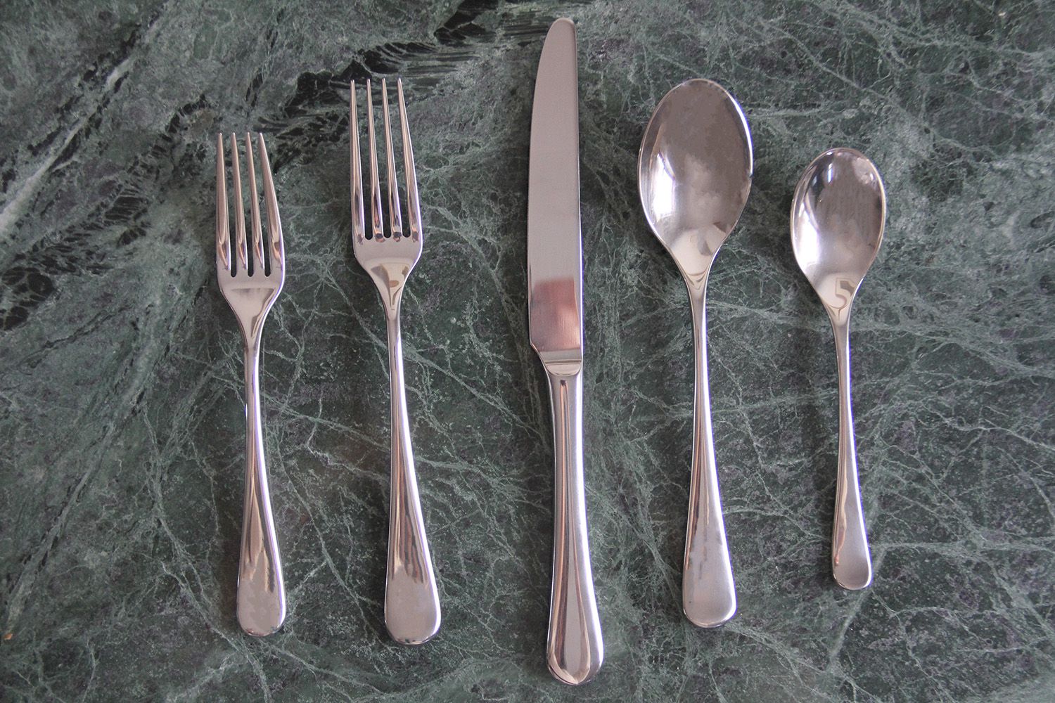 A stainless steel set of silverware on a grey marble surface
