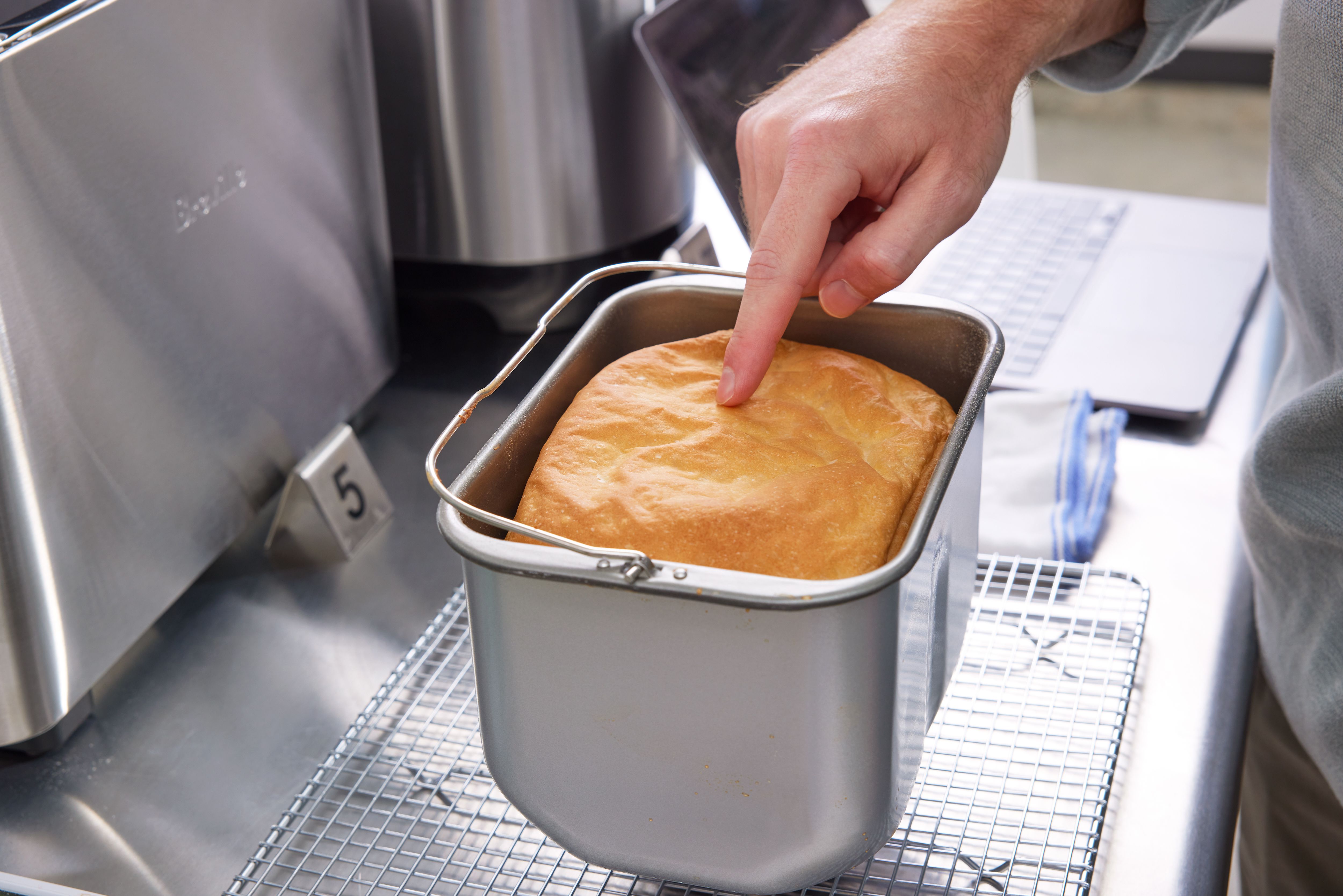 a person pokes the top of a loaf of bread made in a bread machine