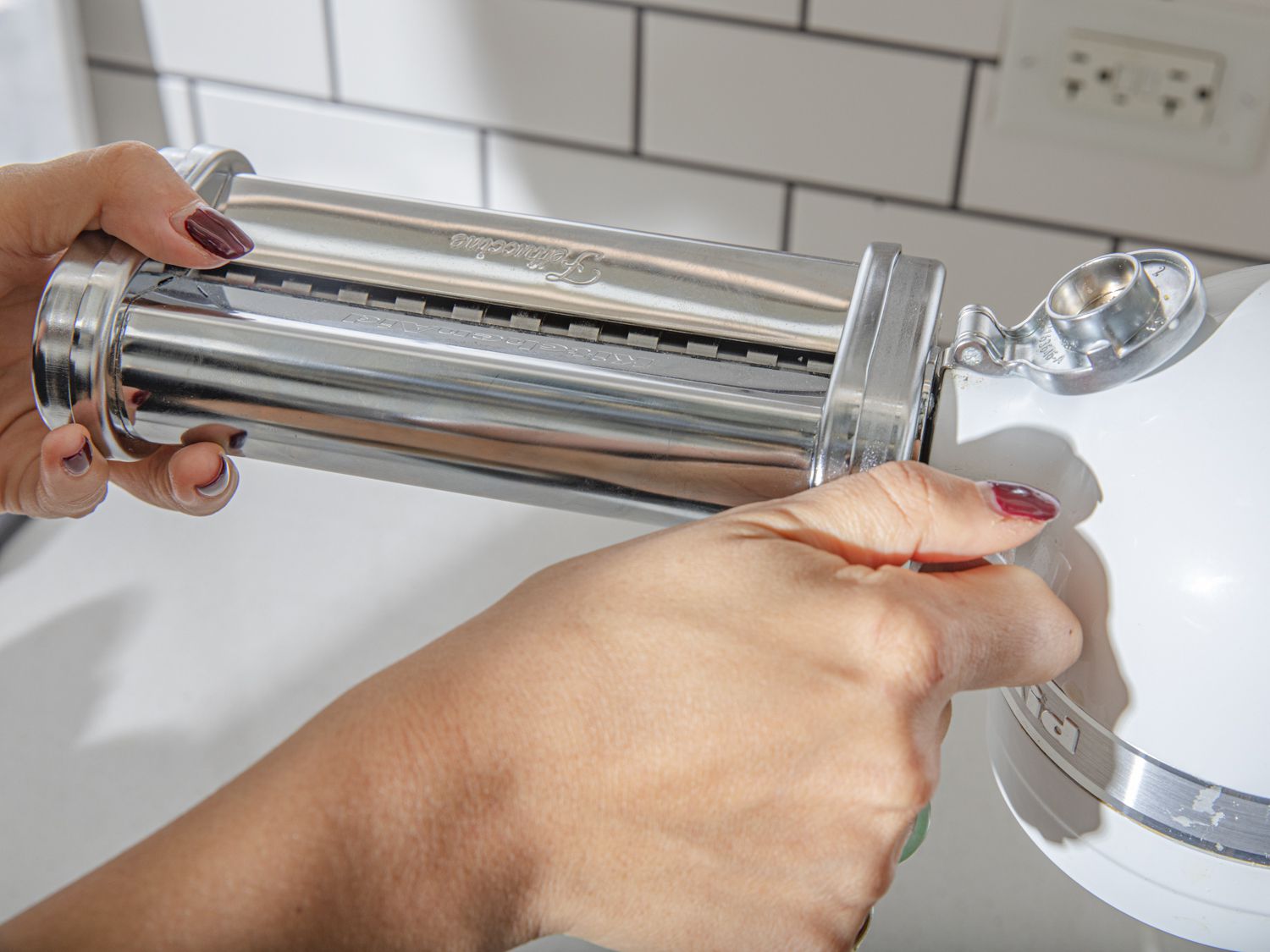 Two hands putting a pasta cutter attachment onto a KitchenAid stand mixer