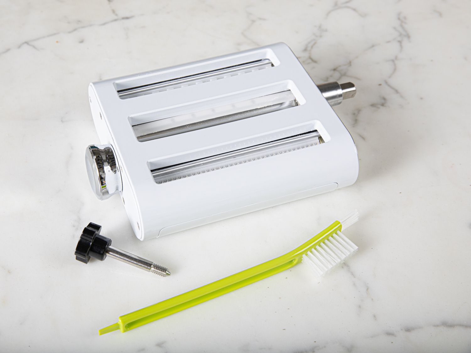 A cleaning brush sitting beside a pasta roller/cutter on a marble surface