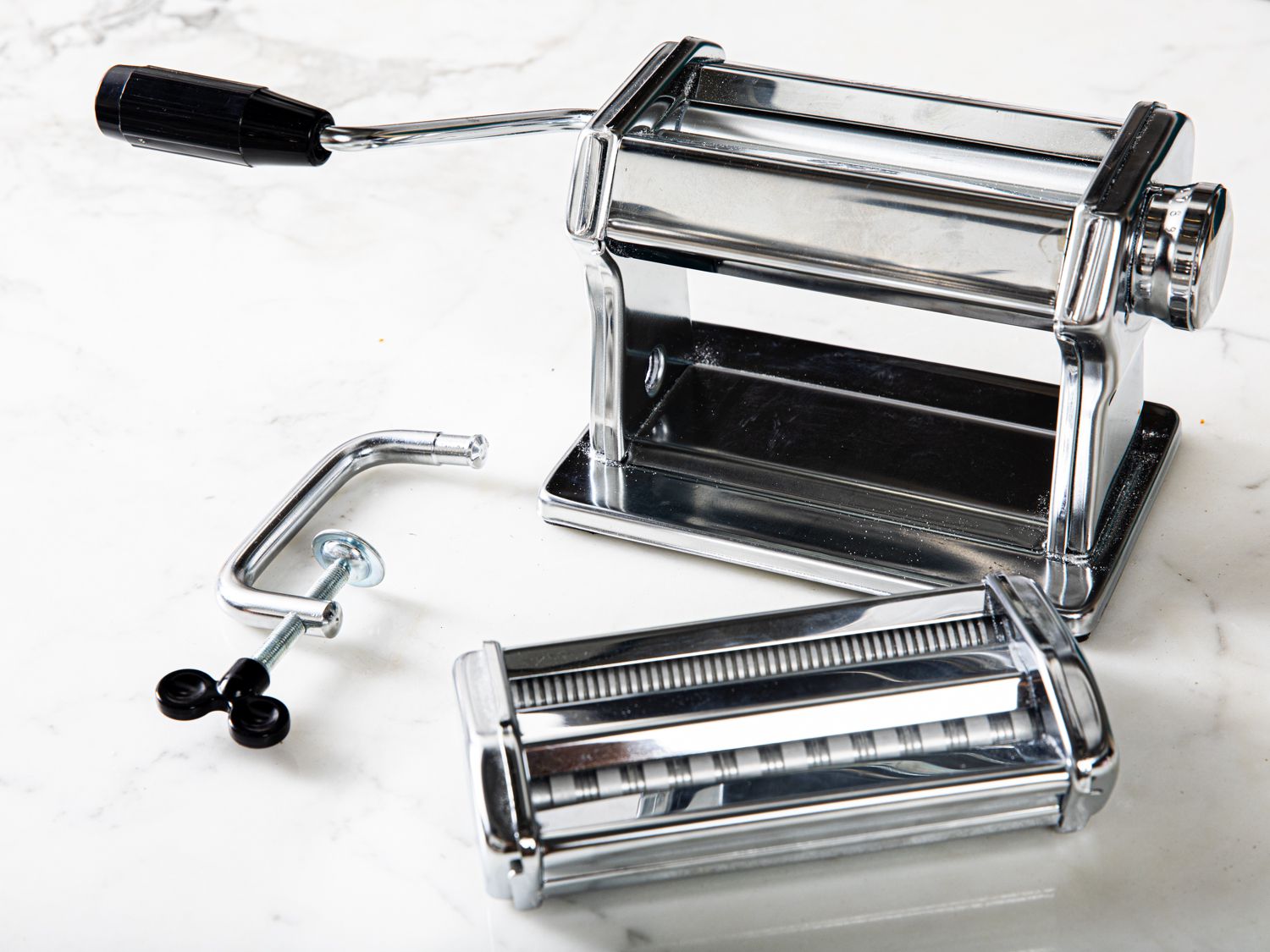 A stainless steel pasta maker with its handle attached on a marble surface