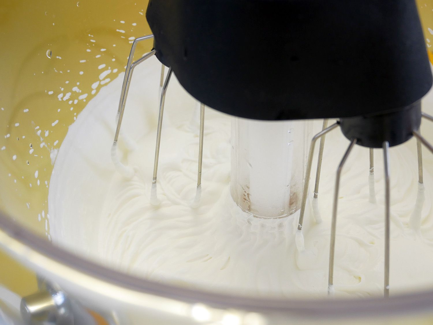 closeup shot of whipped cream in plastic bowl with multi-pronged beaters.