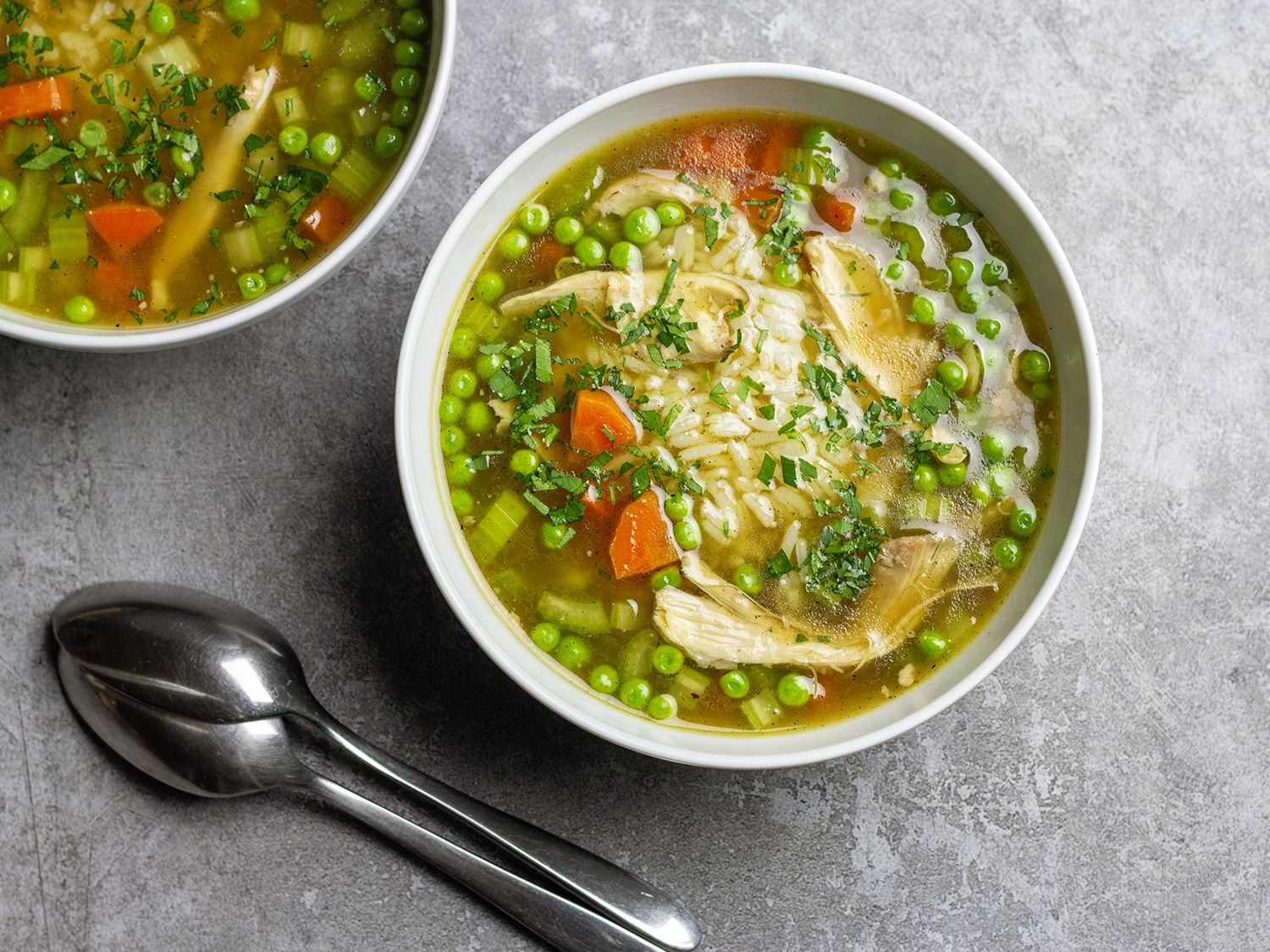Chicken and rice soup fills two white bowls. Two spoons lay beside them.