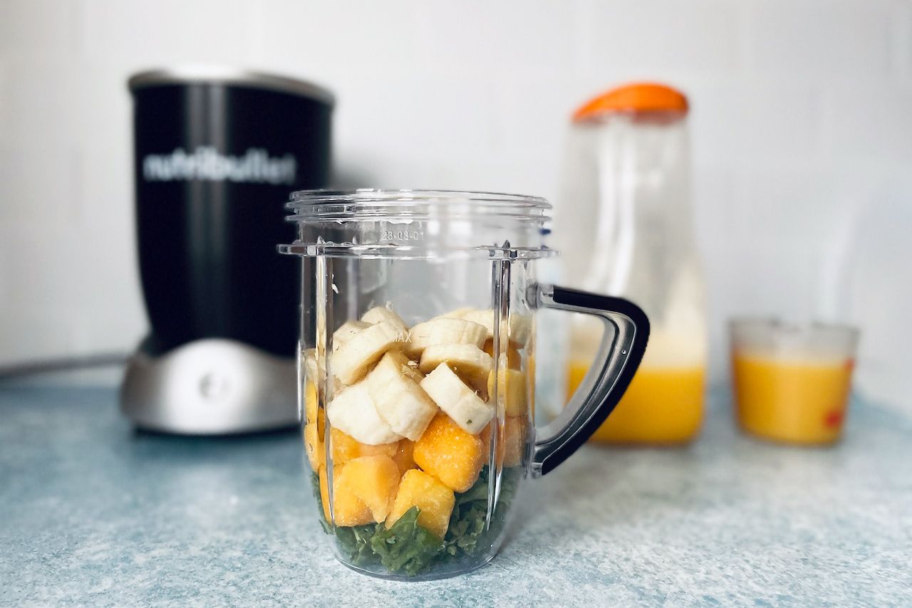 bananas, frozen mango, and kale in a blender jar with blender and orange juice in the background.